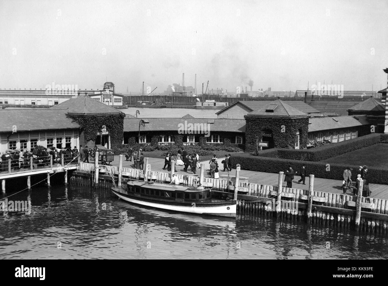 Black and white photograph of buildings near Ellis Island pier, immigrants can be seen on the boardwalk with trunks and luggage, by Edwin Levick, Ellis Island, New York, 1907. From the New York Public Library. Stock Photo
