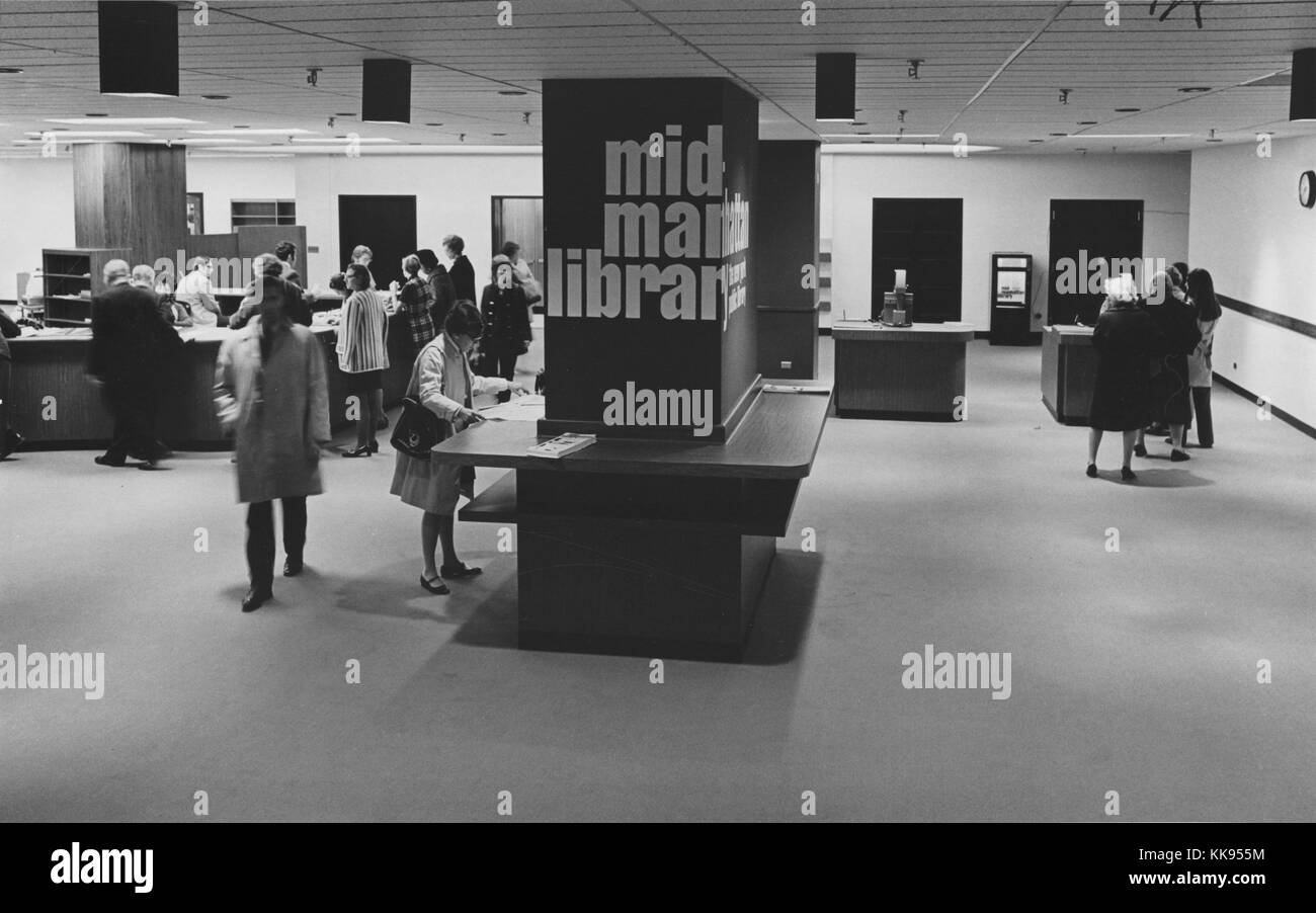 Black and white photograph of the interior of the entrance to the Mid-Manhattan Library, part of the New York Public Library, front desk and people can be seen in the background, New York City, New York, 1970. From the New York Public Library. Stock Photo