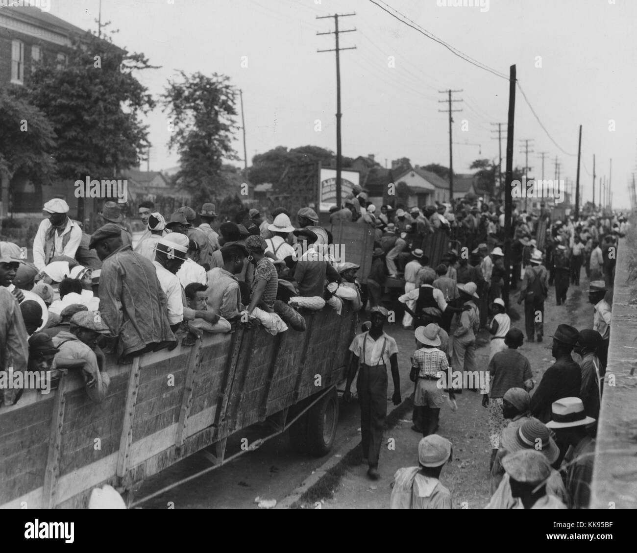 Black and white photograph of a large group of cotton hoers loading into open wagons at Memphis for the day's work in Arkansas, June, 1937. From the New York Public Library. Stock Photo