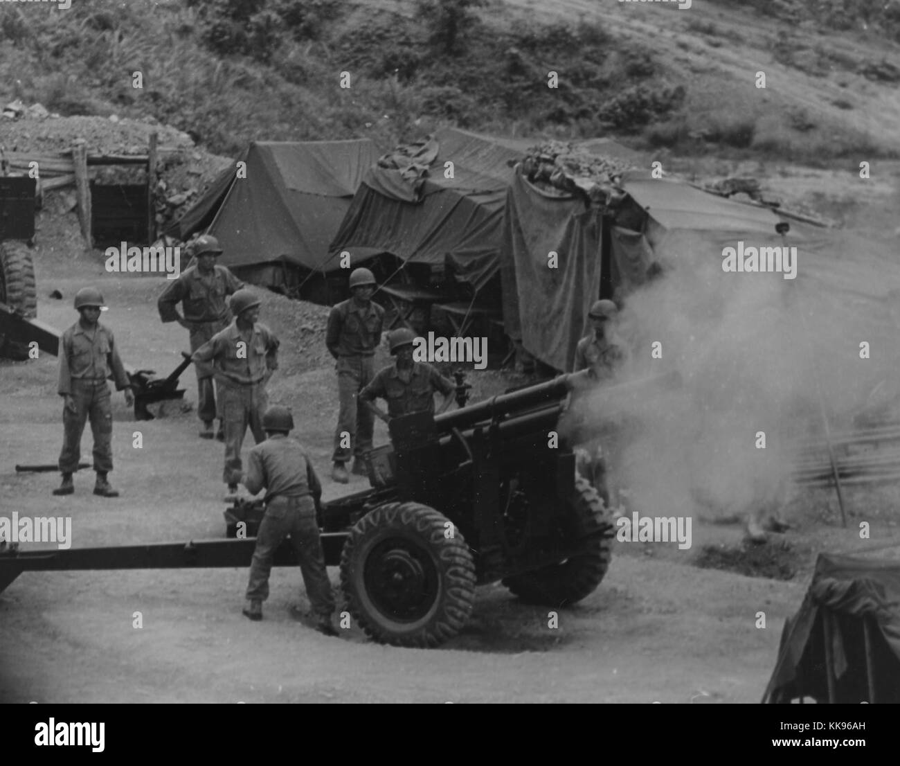 Black and white photograph of a group of Vietnamese artillerymen firing from a mountain position during field training, tents in the background, 1962. From the New York Public Library. Stock Photo