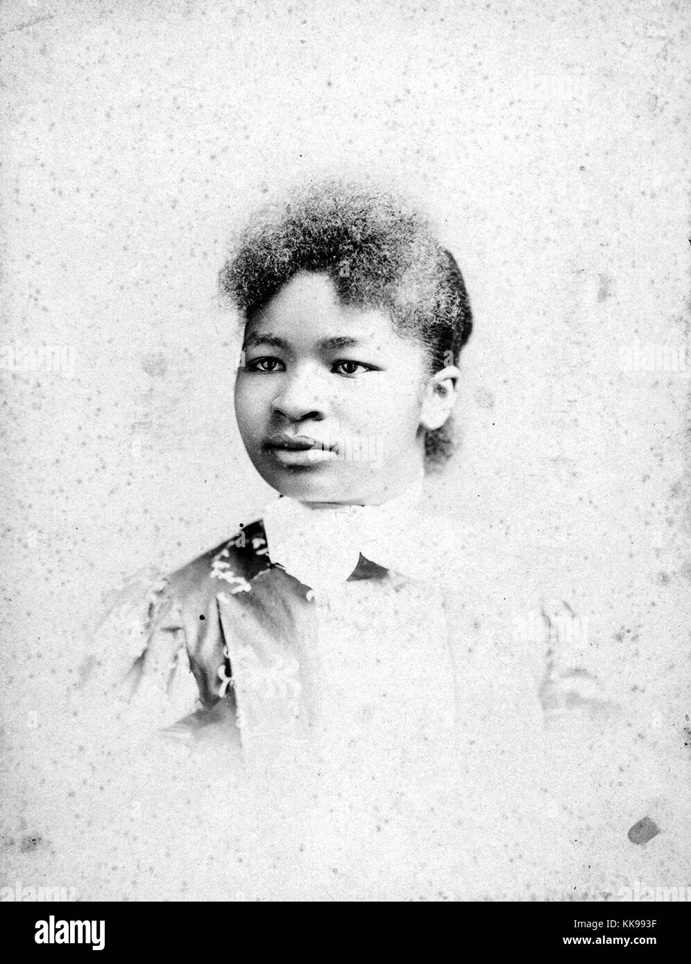 A photographic portrait of an unidentified woman, she is wearing a shirt that consists of a patterned, lustrous, dark-colored fabric and has a white color, she is looking towards her right at a 45 degree angle from the camera, 1900. From the New York Public Library. Stock Photo