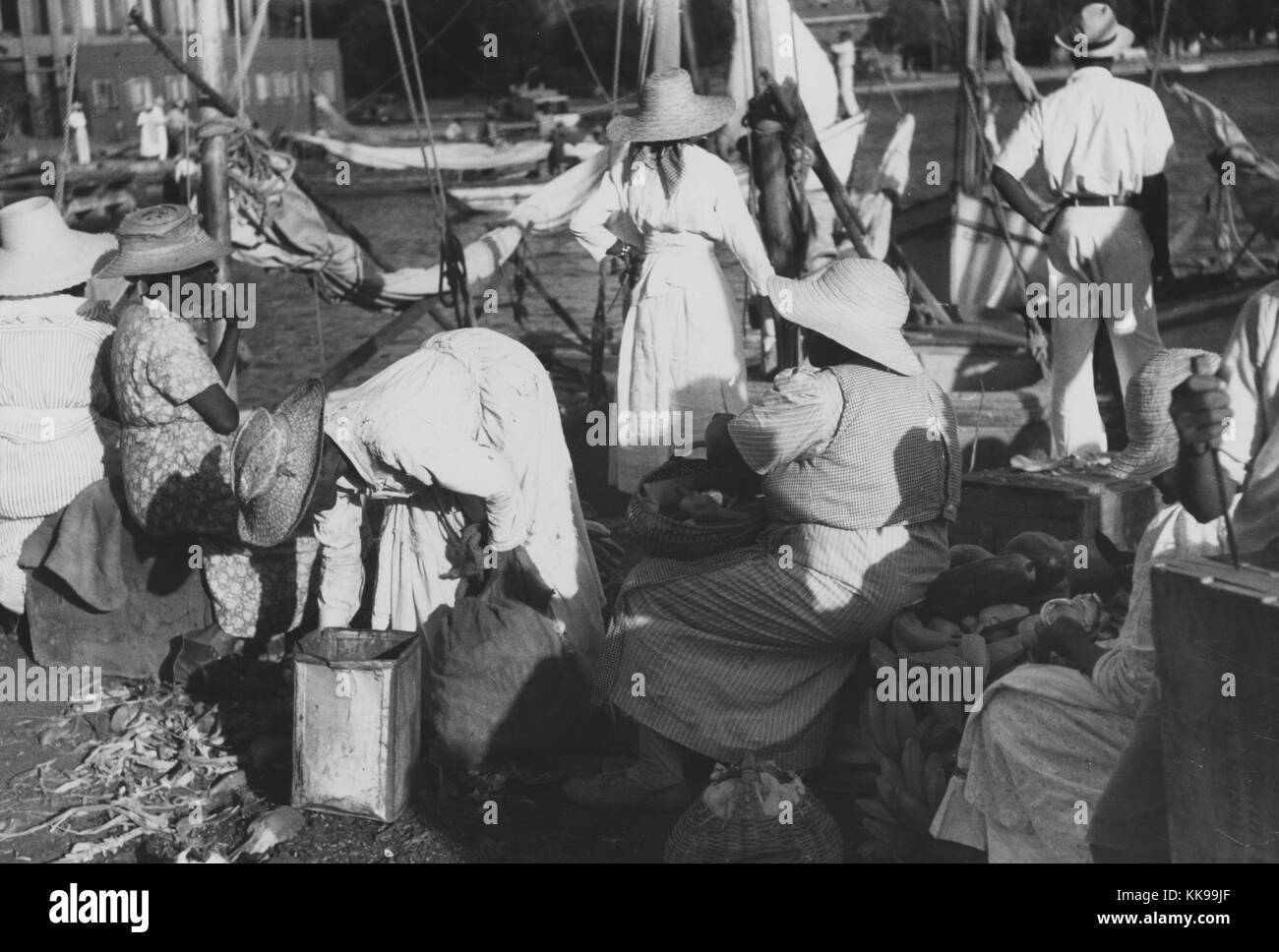 Black and white photograph of a group of women, wearing dresses and wide brimmed hats, selling provisions at Tortola Wharf, Saint Thomas, Virgin Islands, December, 1941. From the New York Public Library. Stock Photo