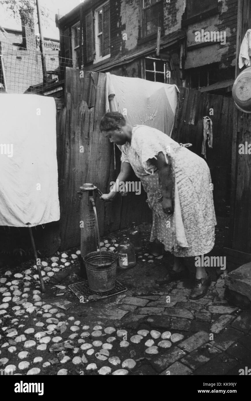 Black and white photograph of a mature African-American woman pumping water into a bucket, outside of a house, Washington, DC, September, 1935. From the New York Public Library. Stock Photo