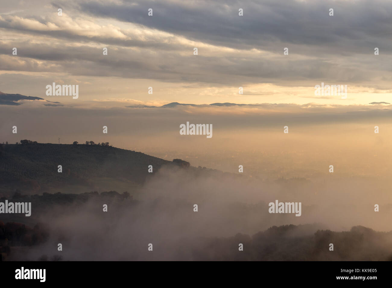 Umbria valley in autumn filled by mist at sunset, with emerging hills and trees and beautiful warm, orange tones Stock Photo