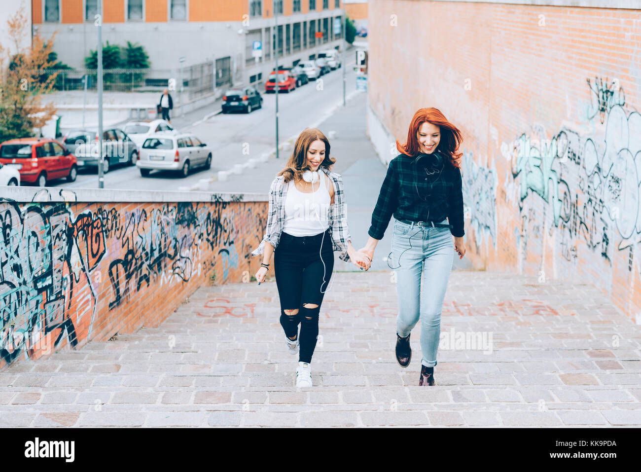 two young women walking outdoors having fun hand in hand - interaction ...