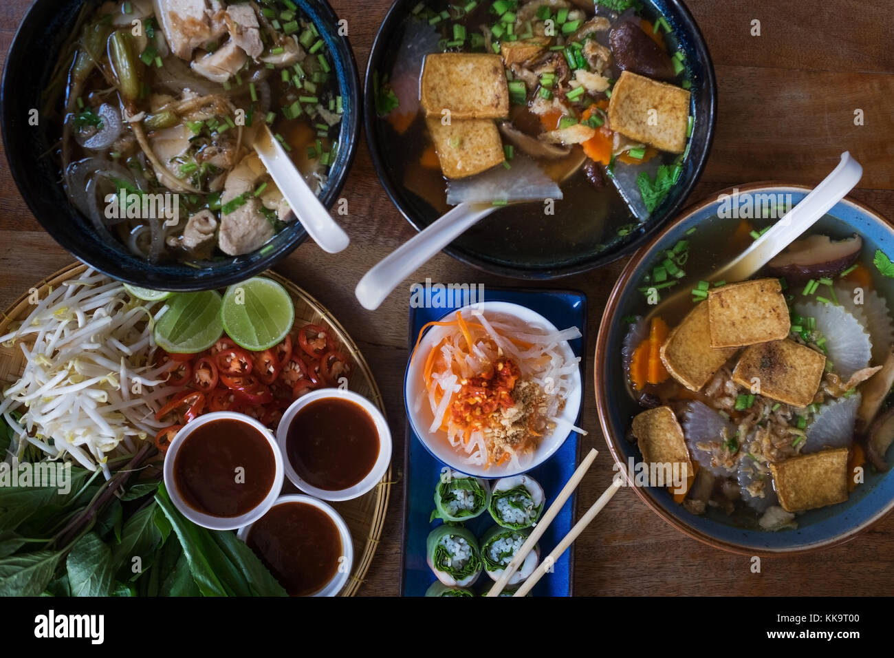 Traditional Vietnamese food. Soups, rolls and fresh herbs. Plates on a wooden surface. Stock Photo
