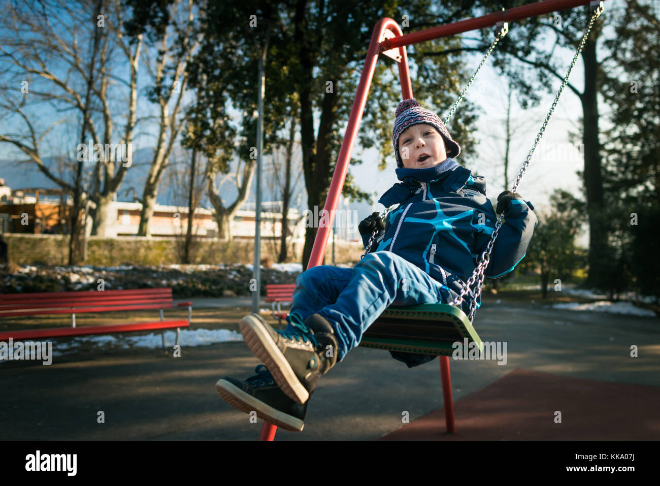 Happy little boy on swing in beautiful winter day have fun and makes faces Stock Photo