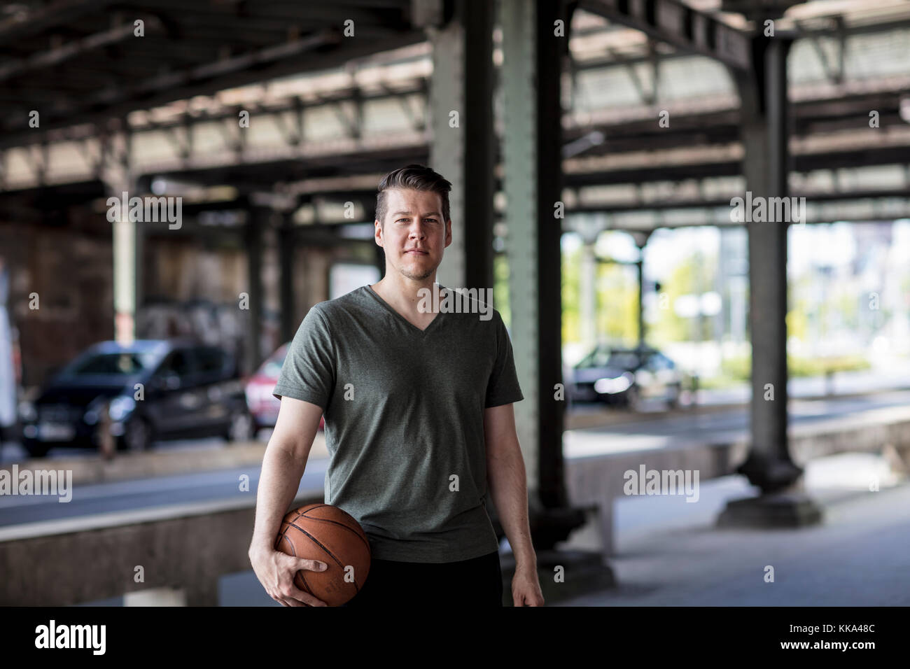Man with a basketball standing under a city bridge. Stock Photo