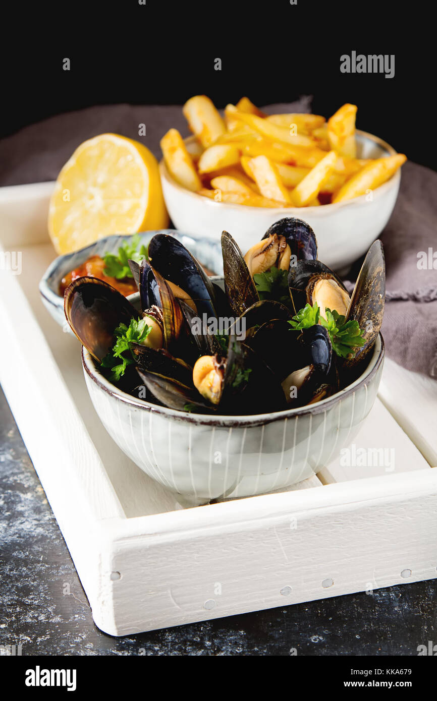 Mussels with herbs in a bowl with lemon and French fries on a white