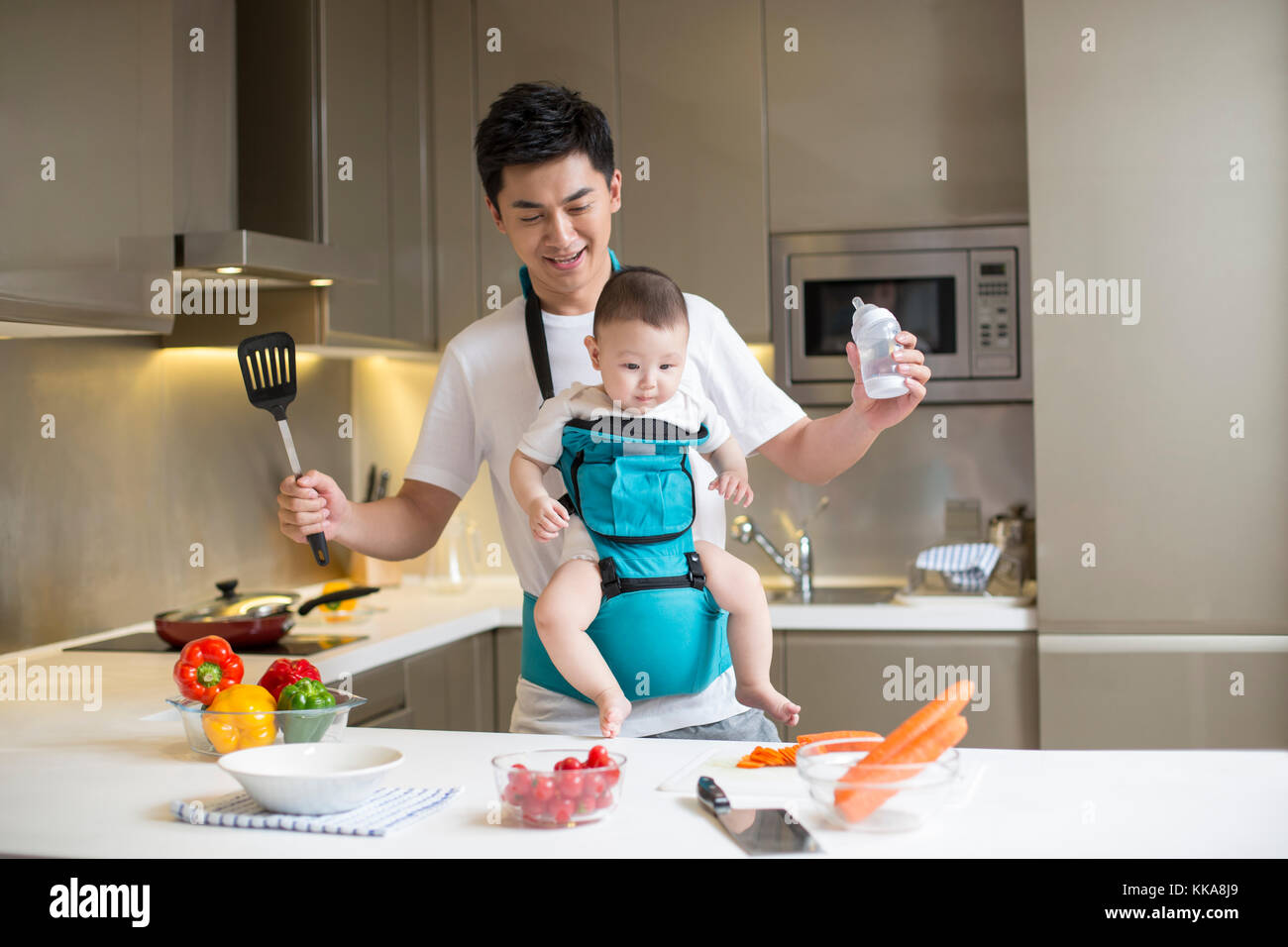 Chinese Father Holding Baby And Cooking In The Kitchen Stock Photo Alamy