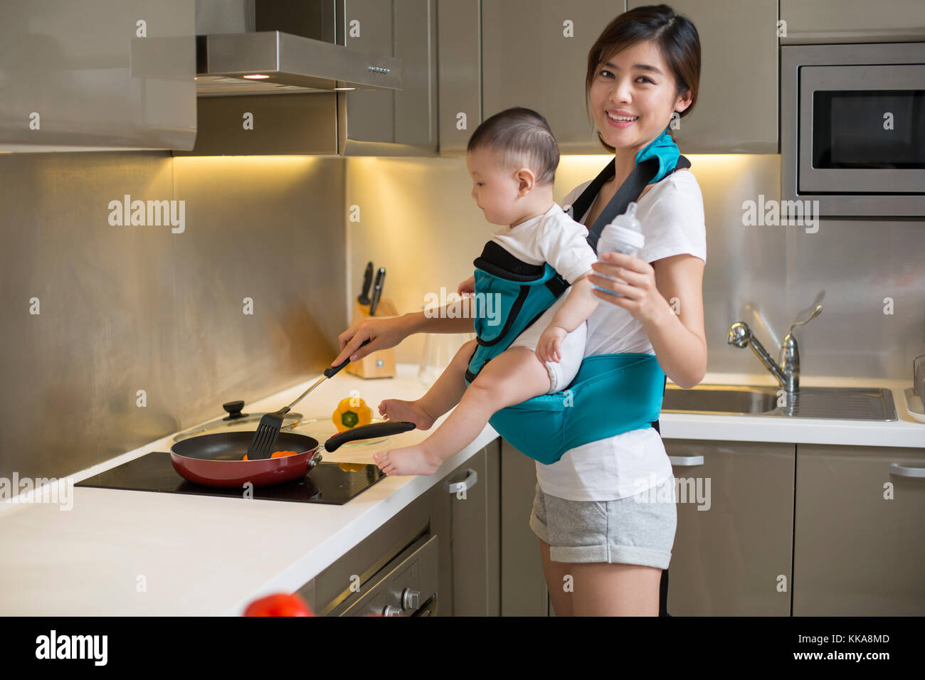 Chinese mother holding baby and cooking in the kitchen Stock Photo