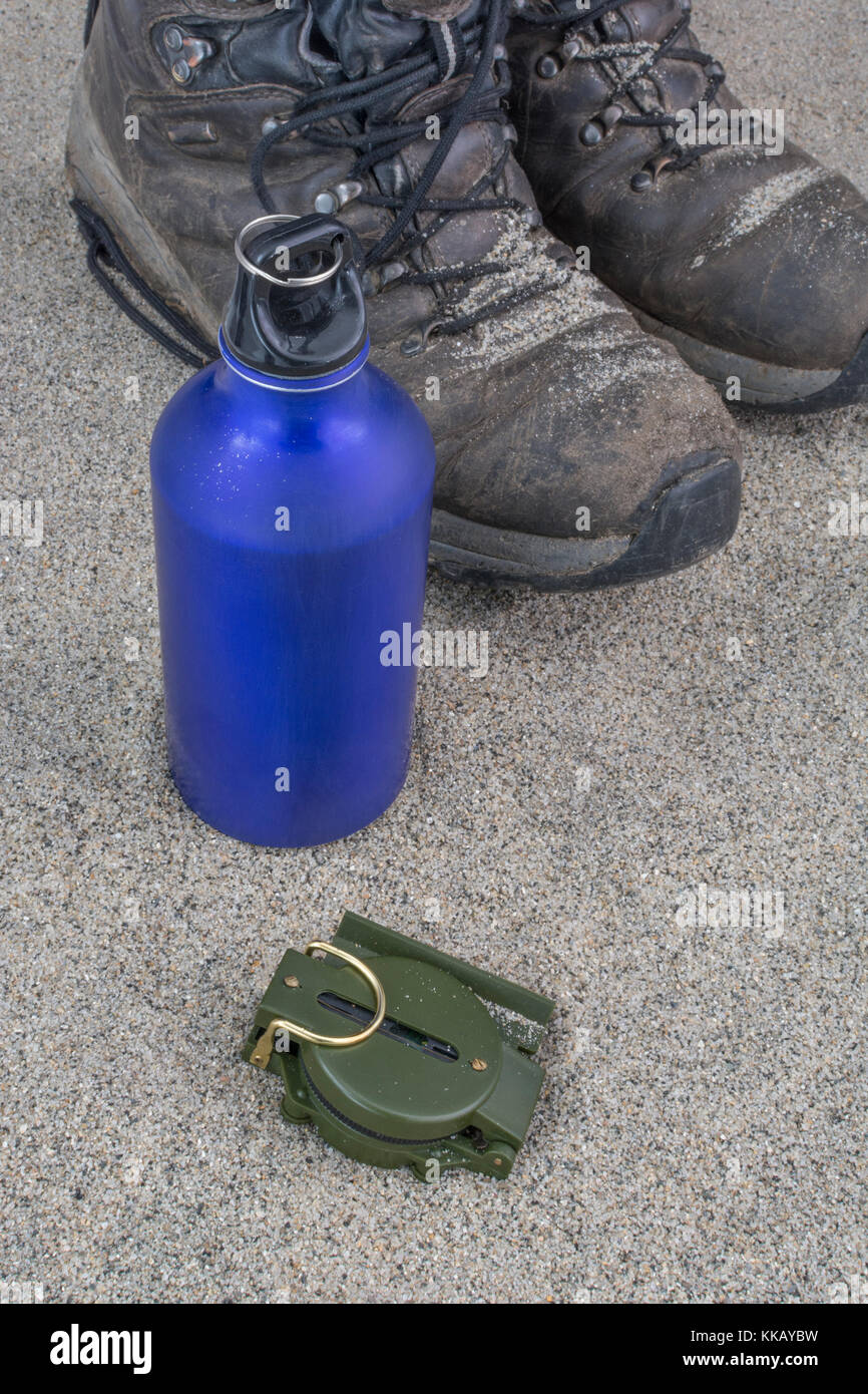 Trekking boots, blue water bottle, and compass - as metaphor for traveling and backpacking in desert or arid zones. Stock Photo