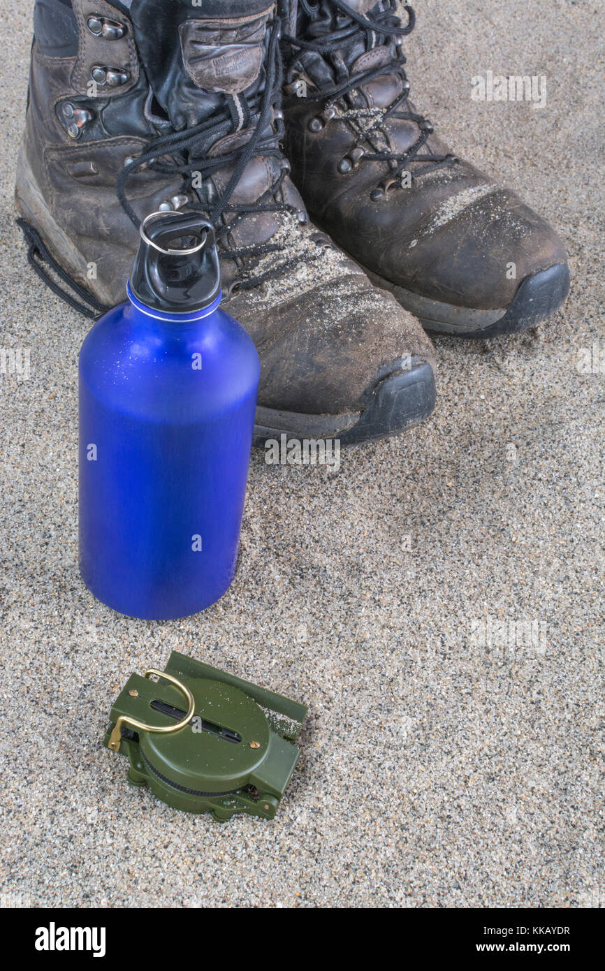 Trekking boots, blue water bottle, and compass - as metaphor for traveling and backpacking in desert or arid zones. Stock Photo