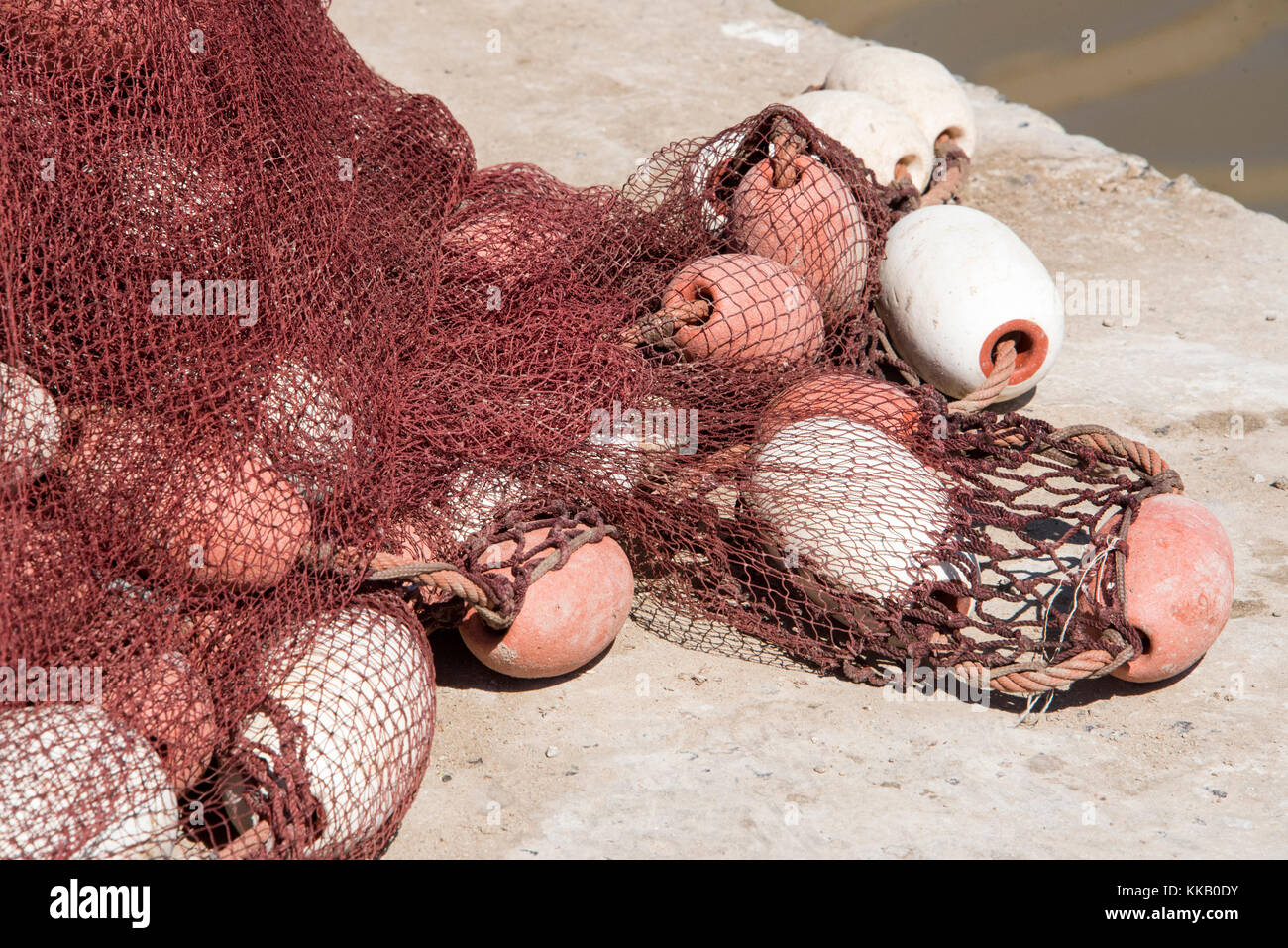 Red nylon fishing nets drying in the sun on the side of the harbour Stock Photo