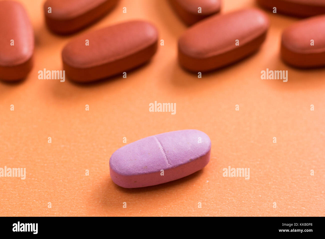 Heap of brown capsules on orange table. One pink pill is apart, isolated. Difference. Stock Photo