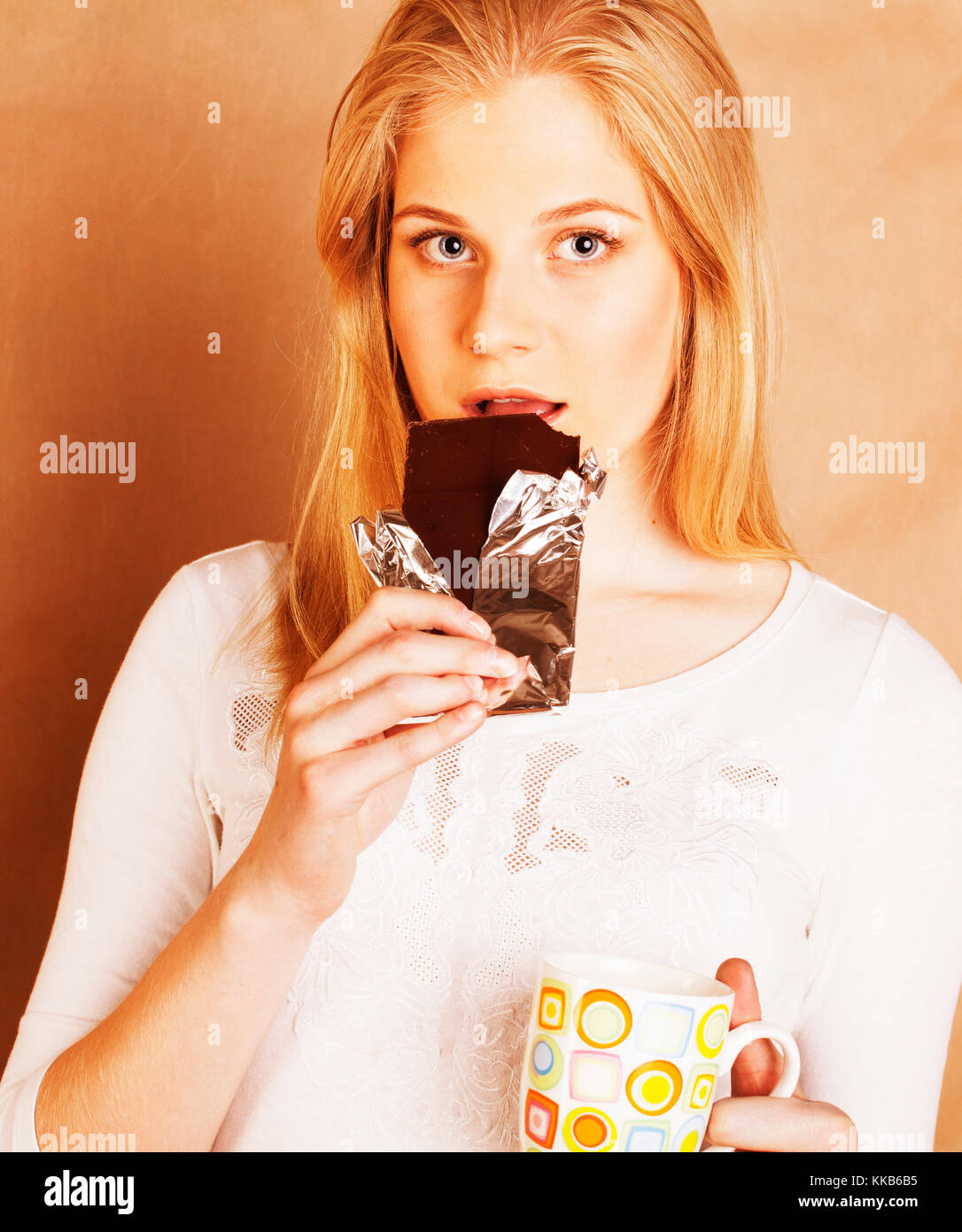 young cute blond girl eating chocolate and drinking coffee close up on