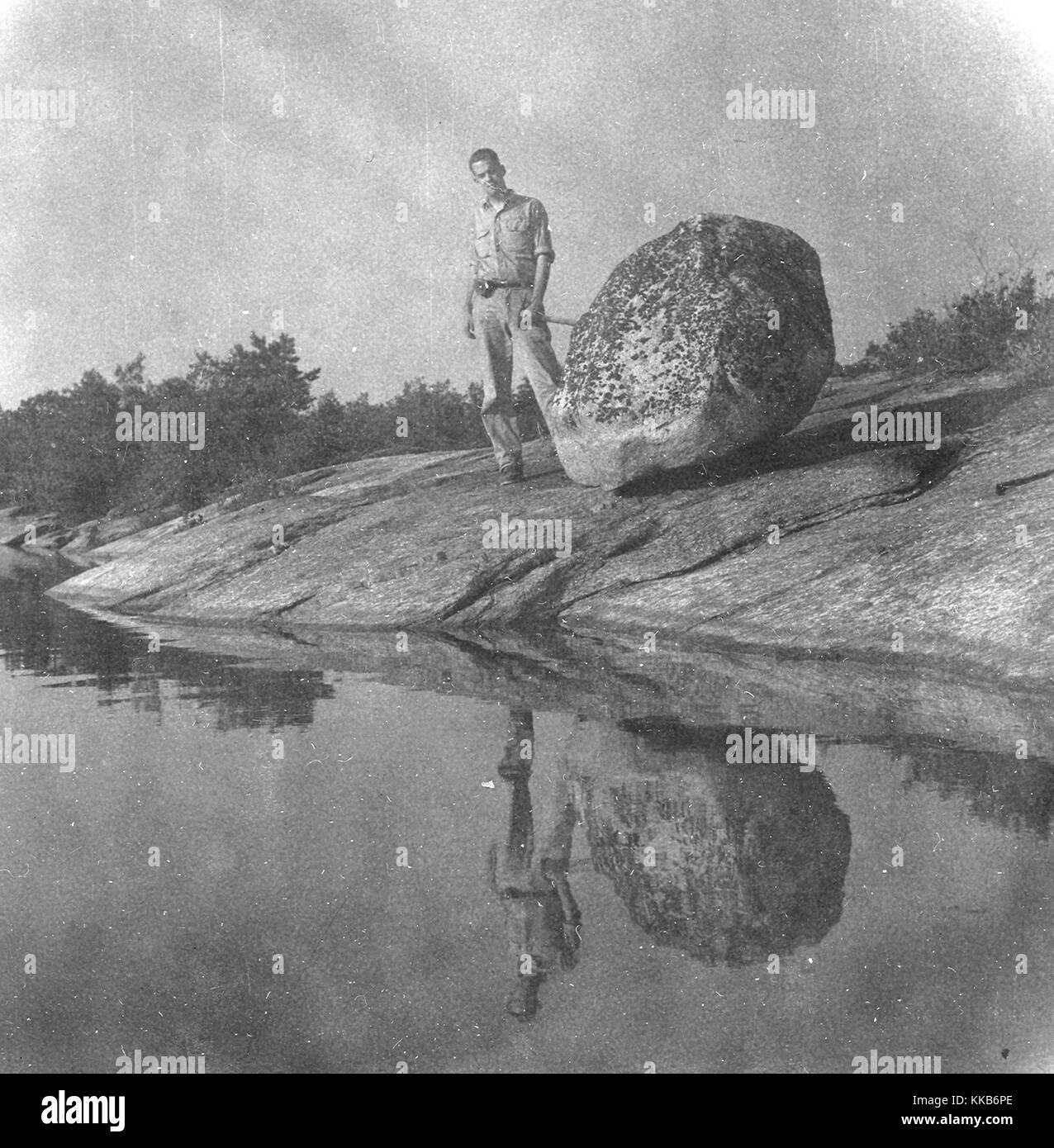 USGS field assistant Robin C. Lease posing with a glacial boulder made of Hope Valley Alaskite Gneiss, Hopkinton, Rhode Island. Image courtesy T.G. Feininger/USGS. July 13, 1962. Stock Photo