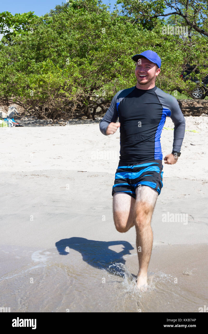 young man running on the hot sand with an obvious tan line on his legs Stock Photo