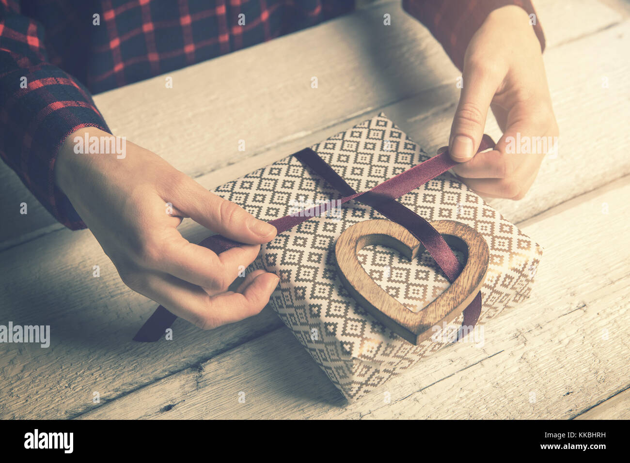 woman wrapping a gift for beloved. tying a ribbon bow with wooden heart