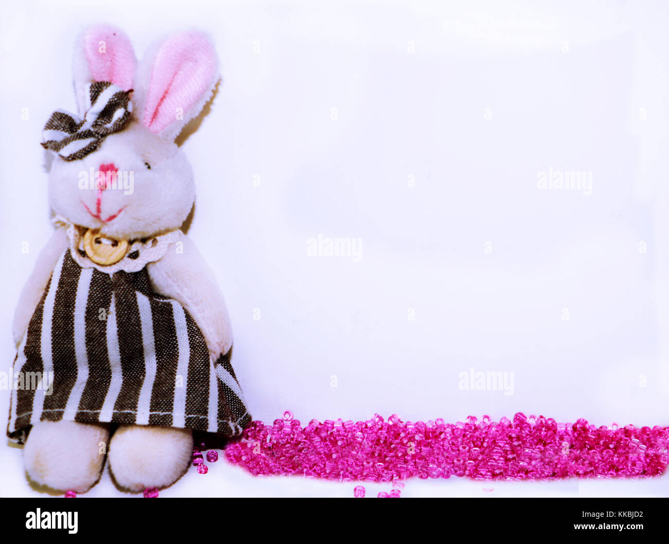 Cute baby frame or template with plush bunny and spilled rose beads and space for text on white background. Stock Photo