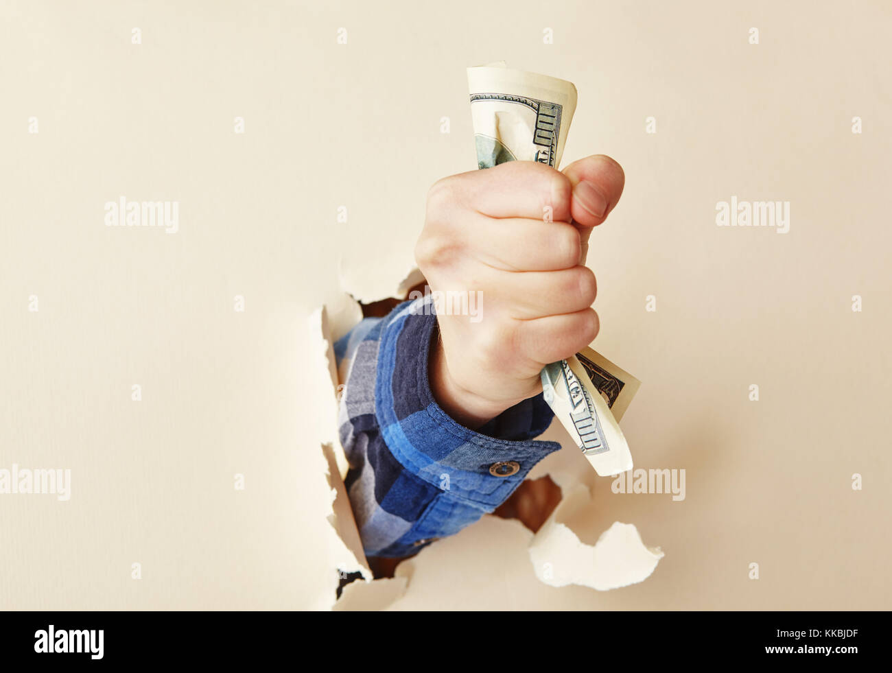 the hand holds a hundred dollar bill through the torn paper Stock Photo