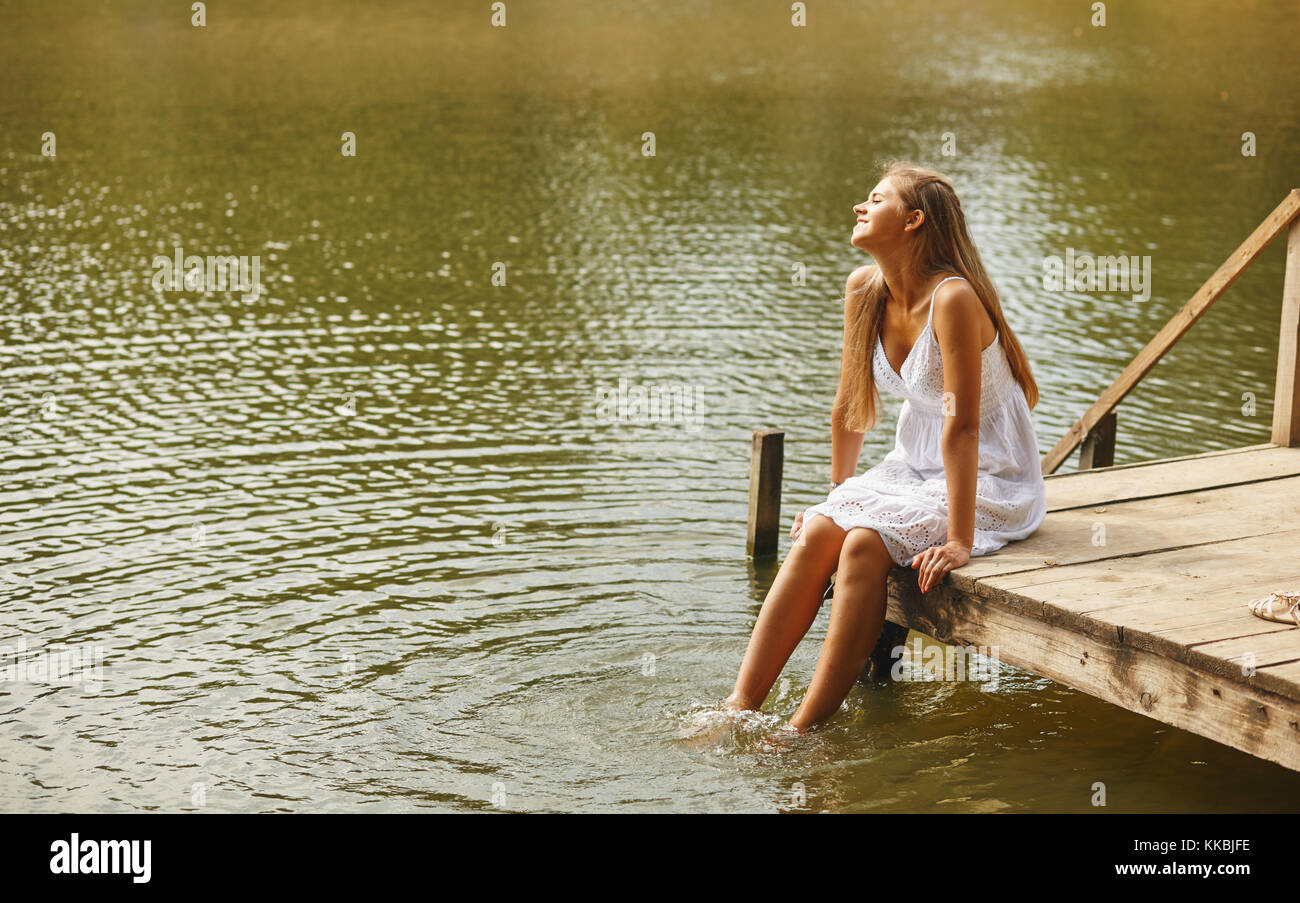 Girl sitting on pier and looking at the river Stock Photo - Alamy
