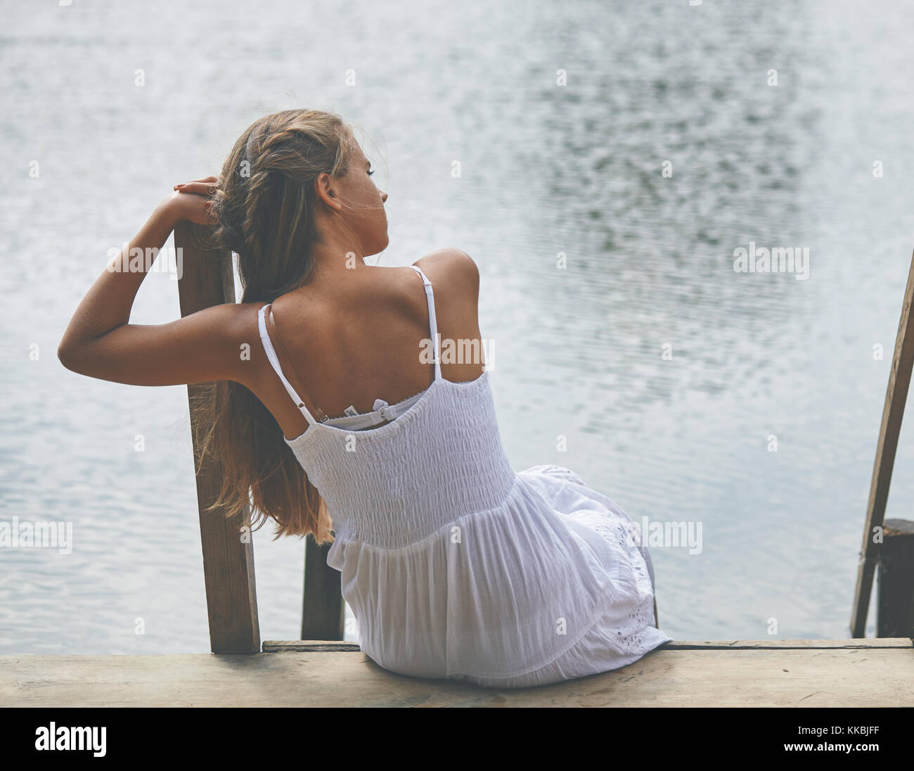 Girl sitting on pier and looking at the river Stock Photo - Alamy