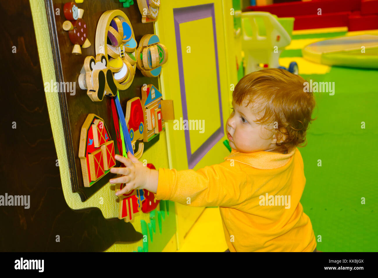cute little baby with ginger hair playing with busyboard in the colored baby room. Stock Photo