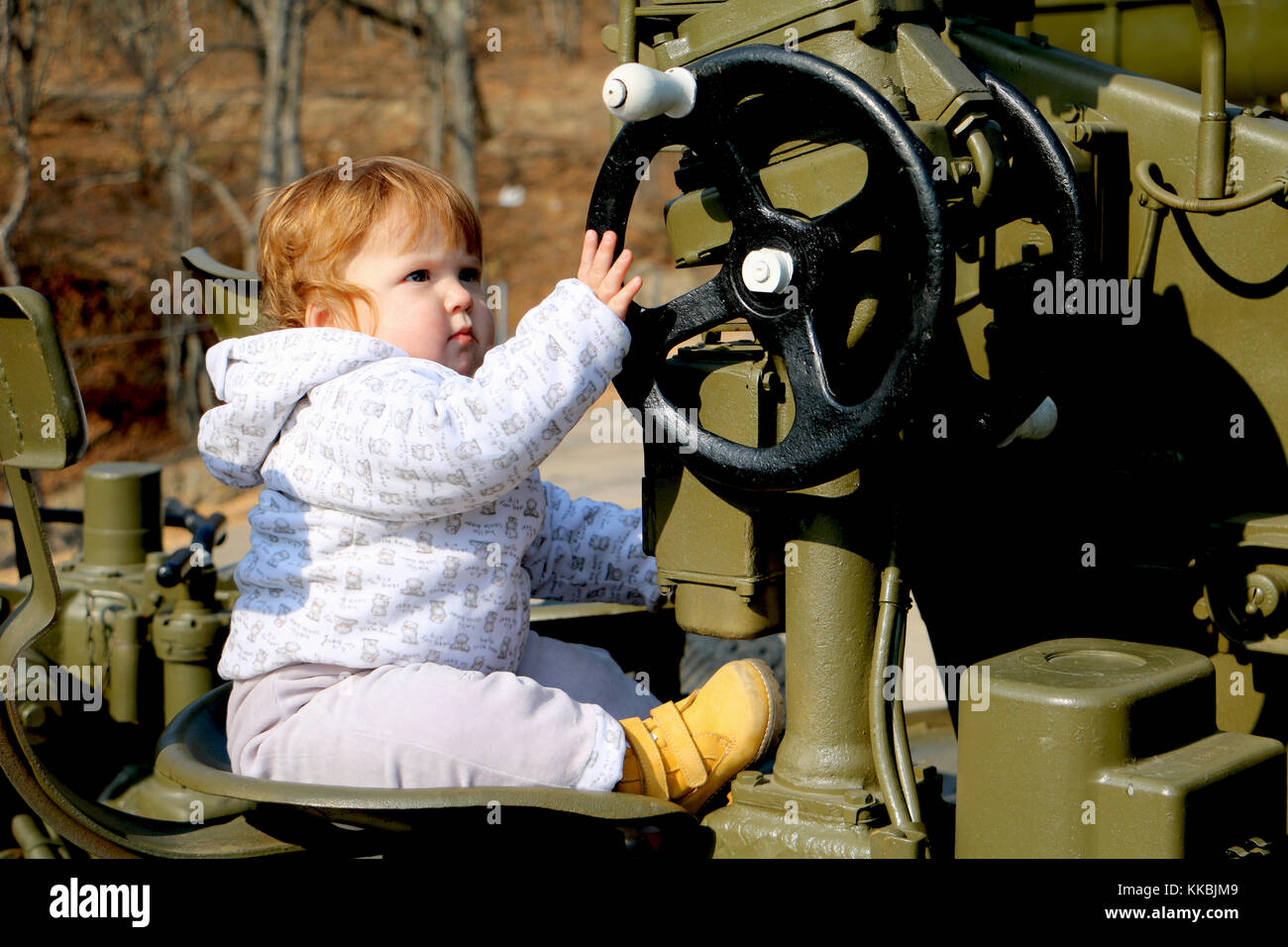 cute ginger baby sitting at the  steering wheel of military army machine. Stock Photo
