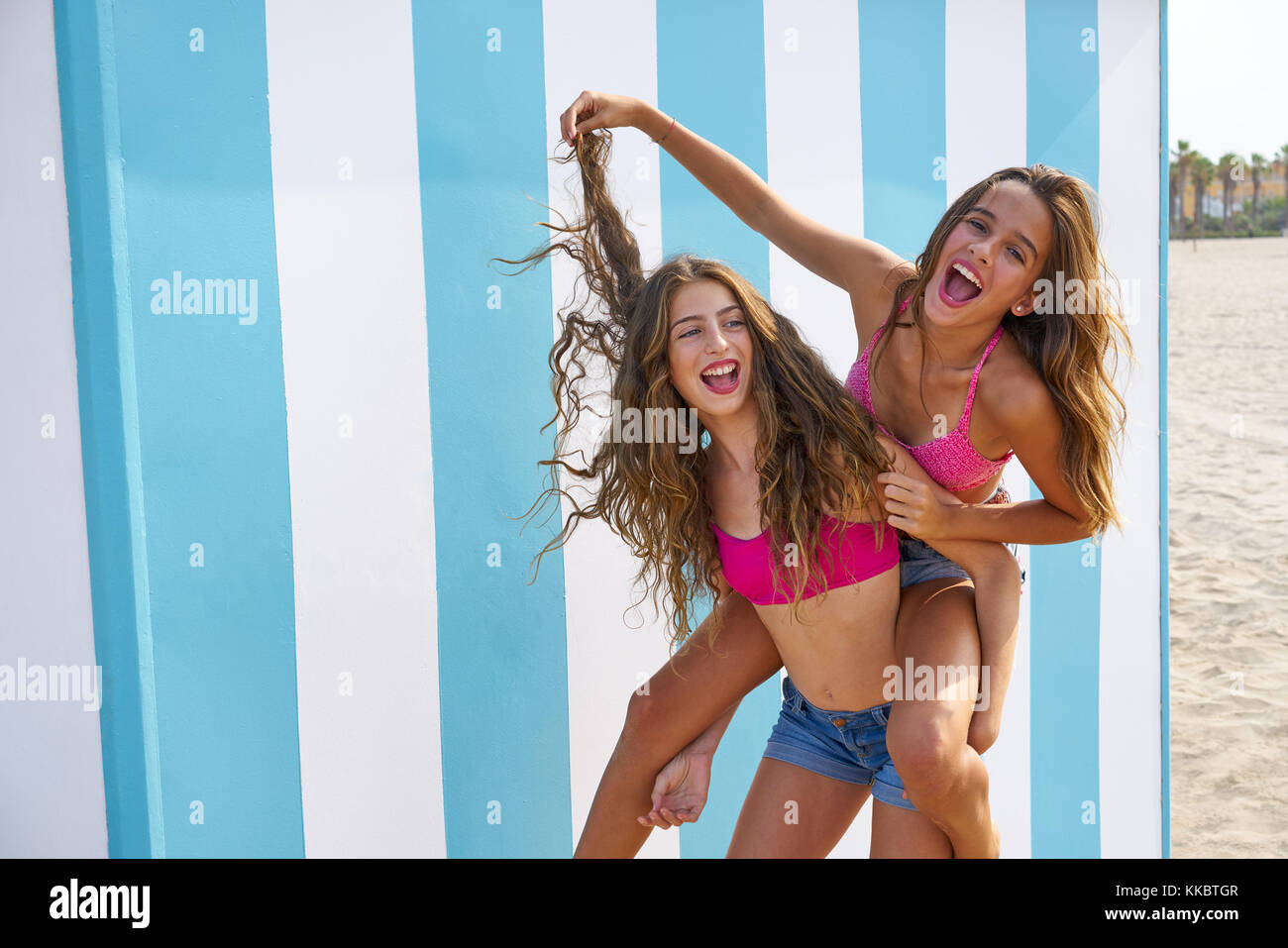 Best friends girls piggyback in summer beach with blue stripes background Stock Photo