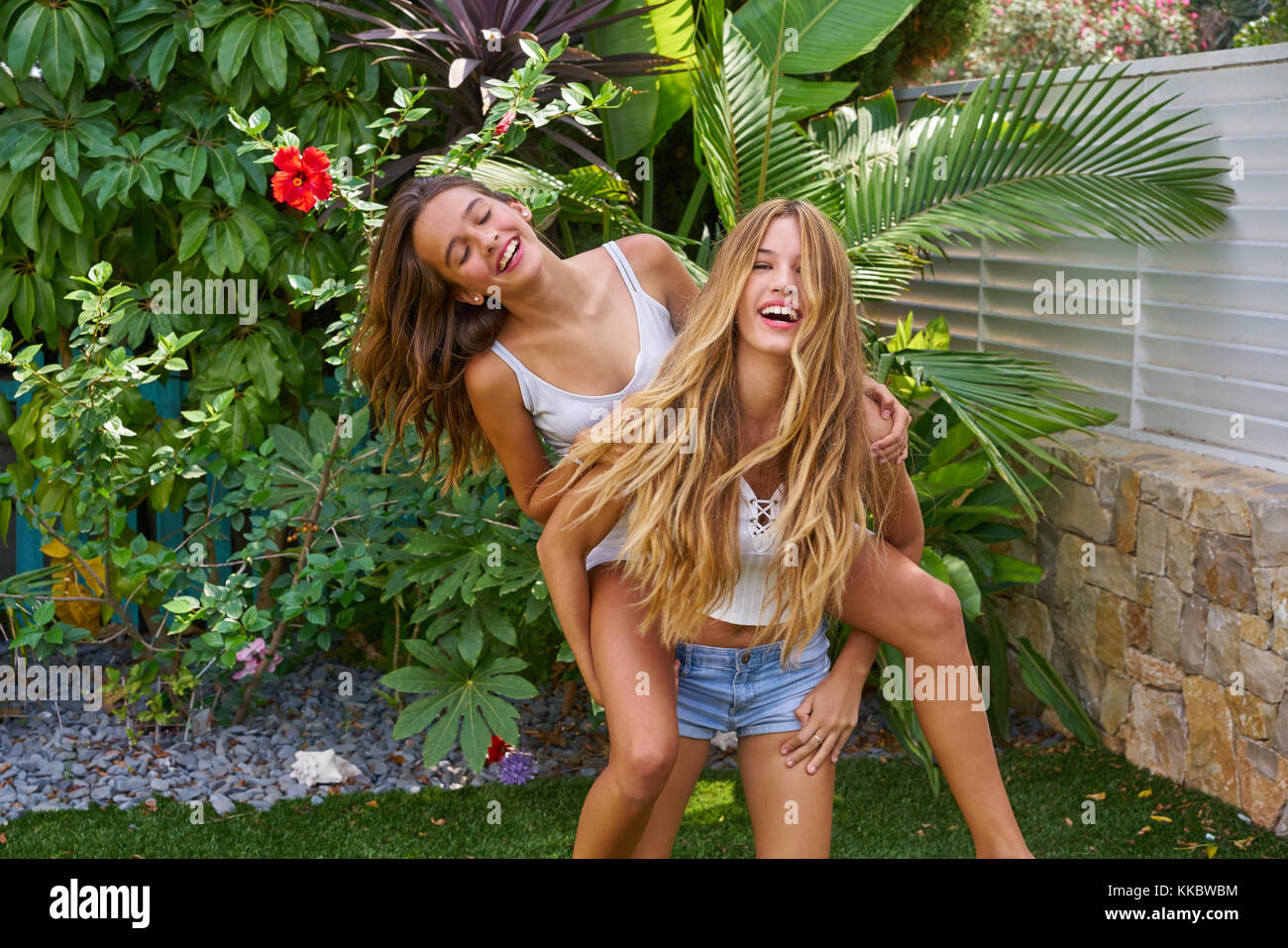 Best friends teen girls piggyback on backyard garden happy smiling Stock Photo