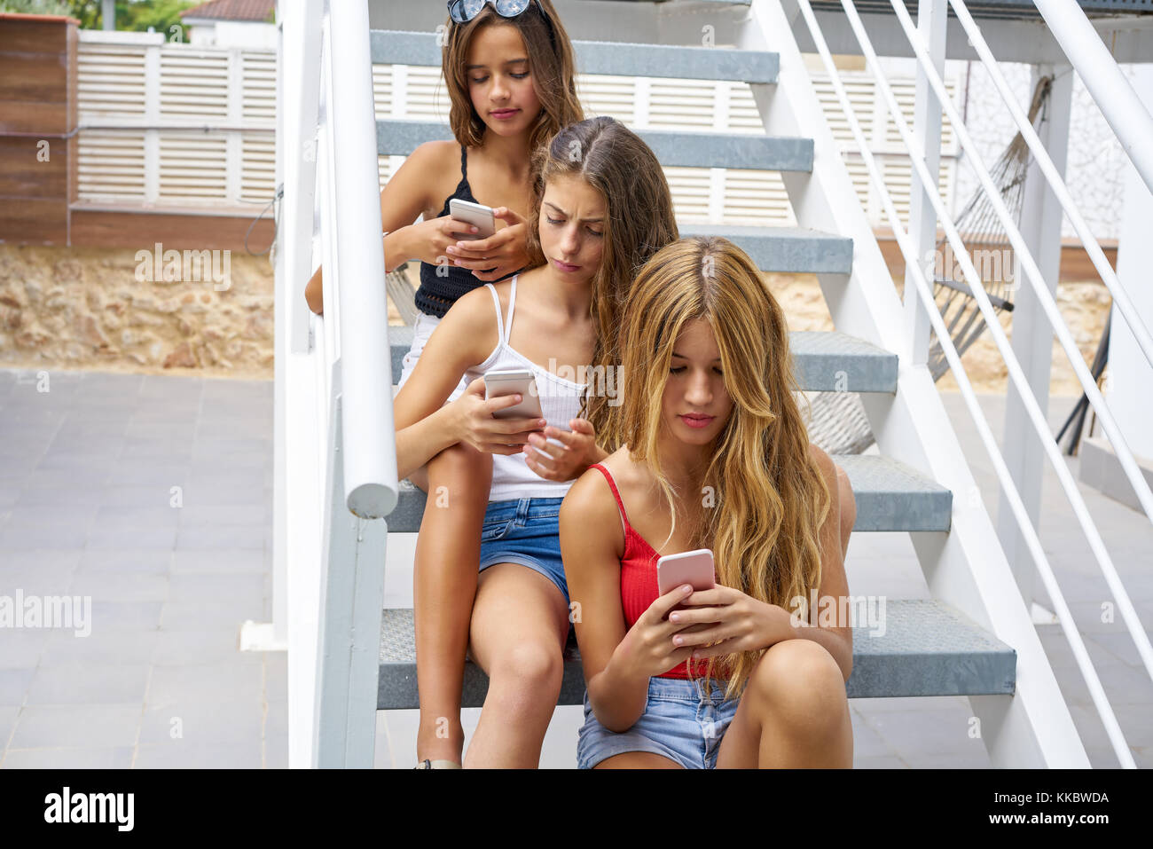 Teen best friends girls in a row with smartphone having fun on stairs Stock Photo