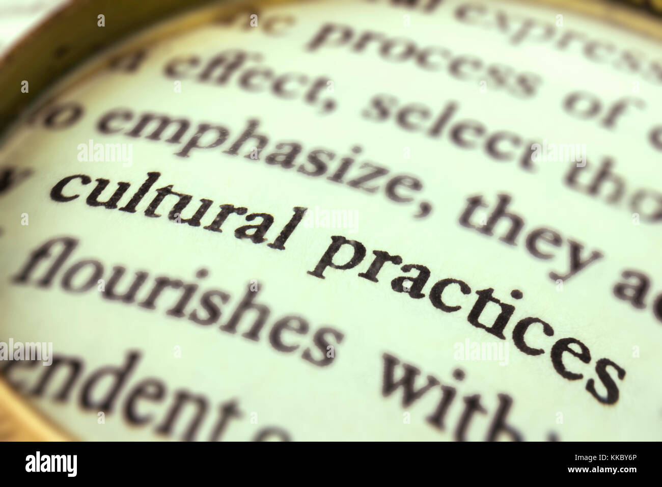 The group of words 'Cultural practices' emphasized by a magnifying glass and wrapped around with a blurry text. Stock Photo