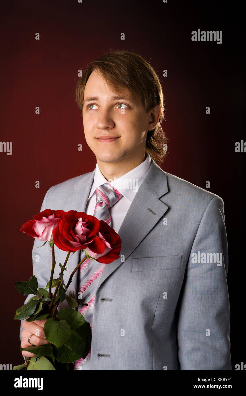 Young man wearing suit holding roses over red background Stock Photo