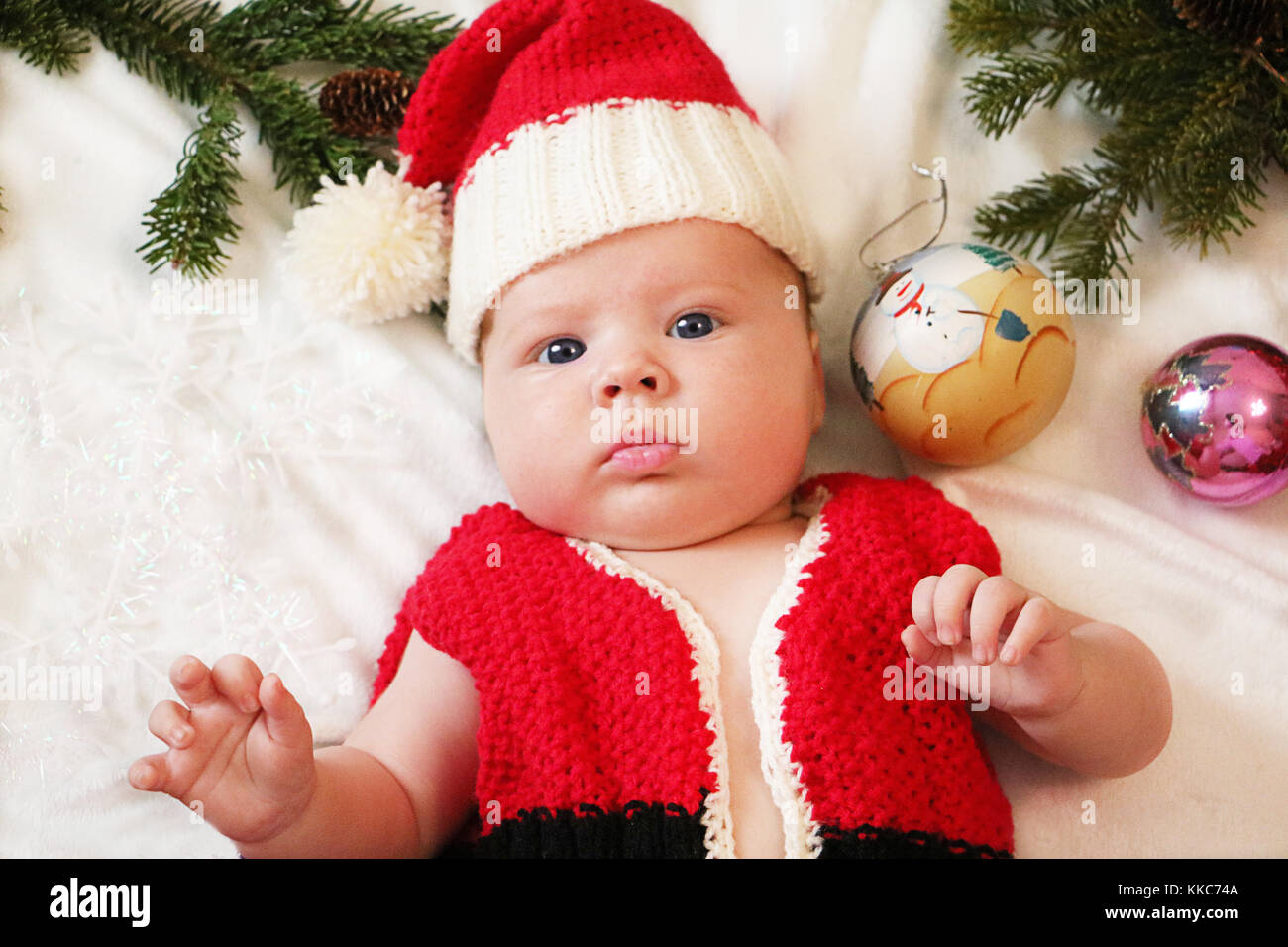 Baby first christmas. Beautiful little baby in Santa hat celebrates Christmas. New Year's holidays. Baby with santa hat inside tinsel, balls and  and  Stock Photo
