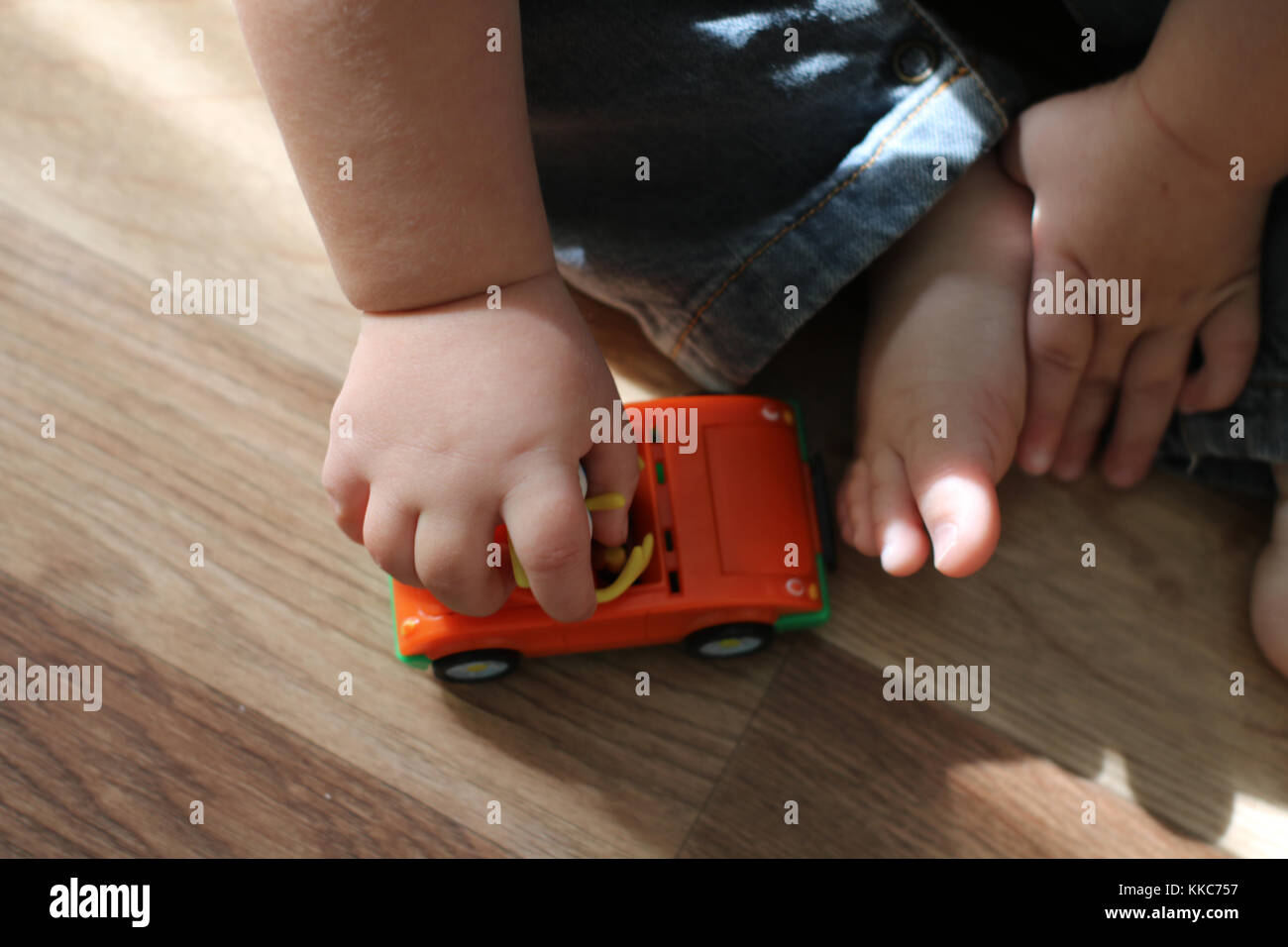 Cute little baby playing with toy car on the floor. Close up baby hands holding toy car and little barefoot feet. Stock Photo