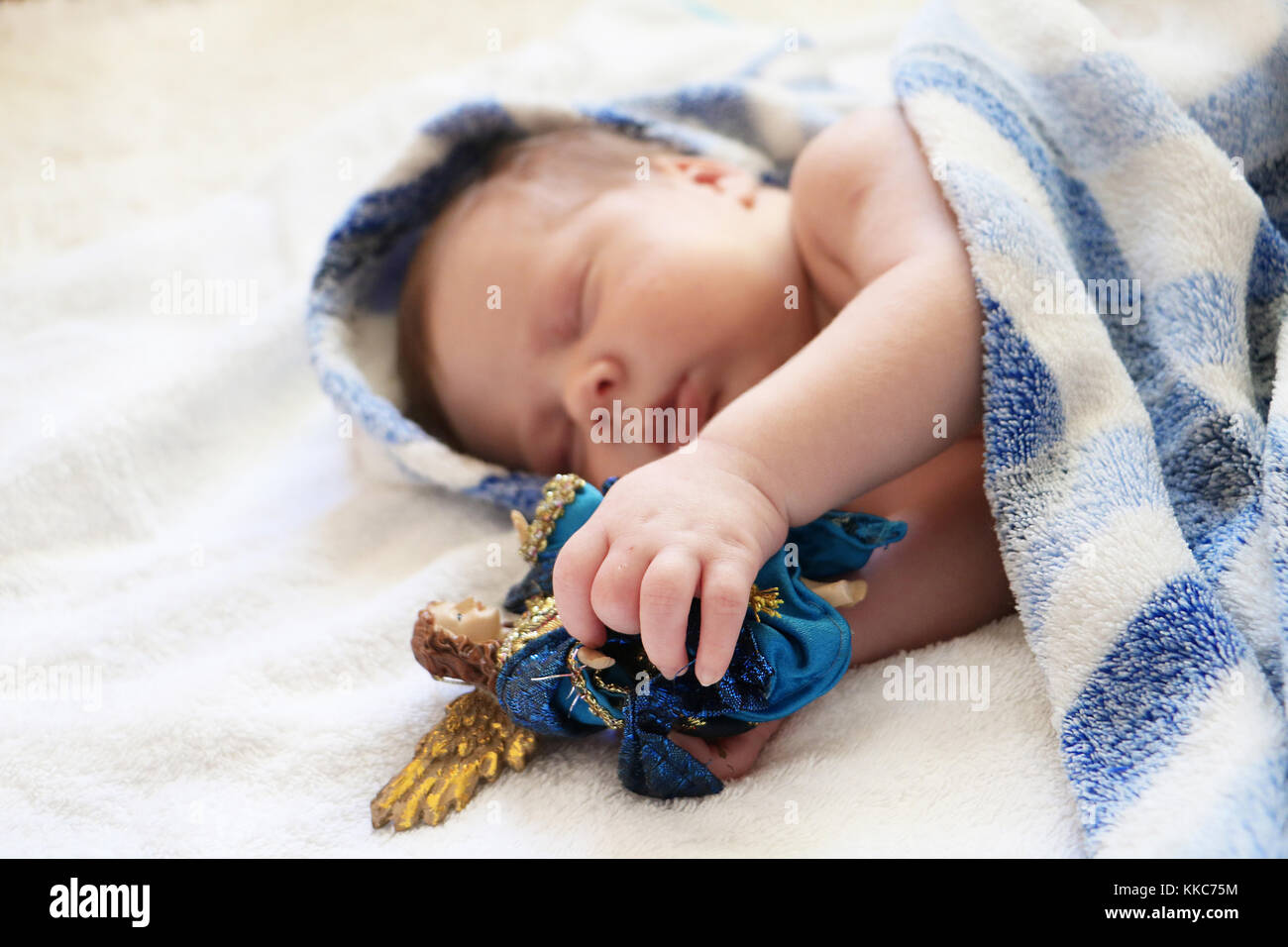 Christmas baby. Portrait of cute newborn baby sleeping in blue blanket with figure of angel in hands on white background. Stock Photo
