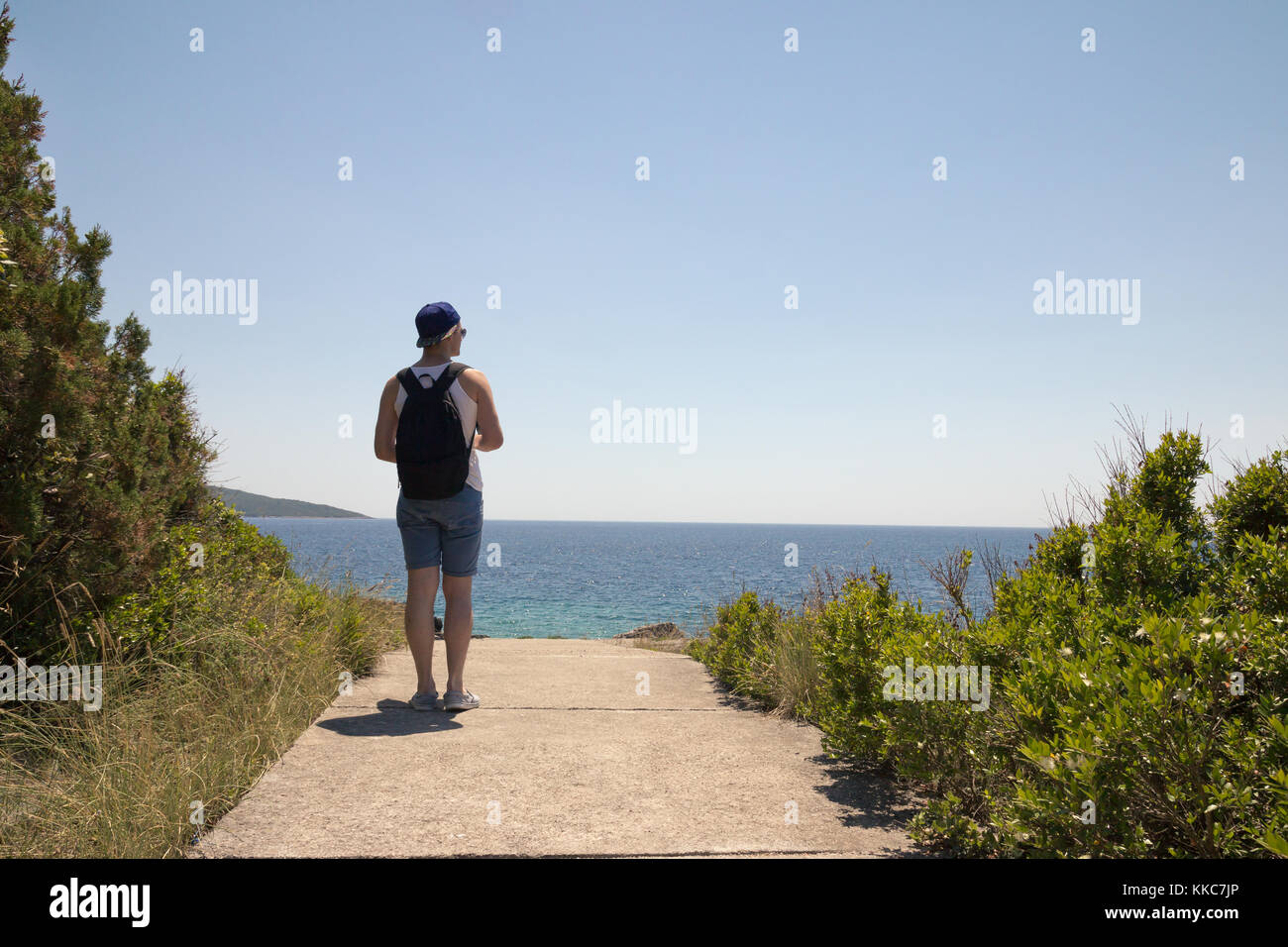 one young man back, rear view, outdoor standing near lake sea, looking at coast. Stock Photo