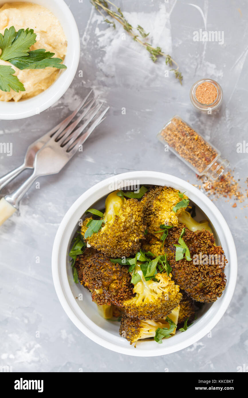 Baked broccoli in white ceramic form with hummus, top view, gray