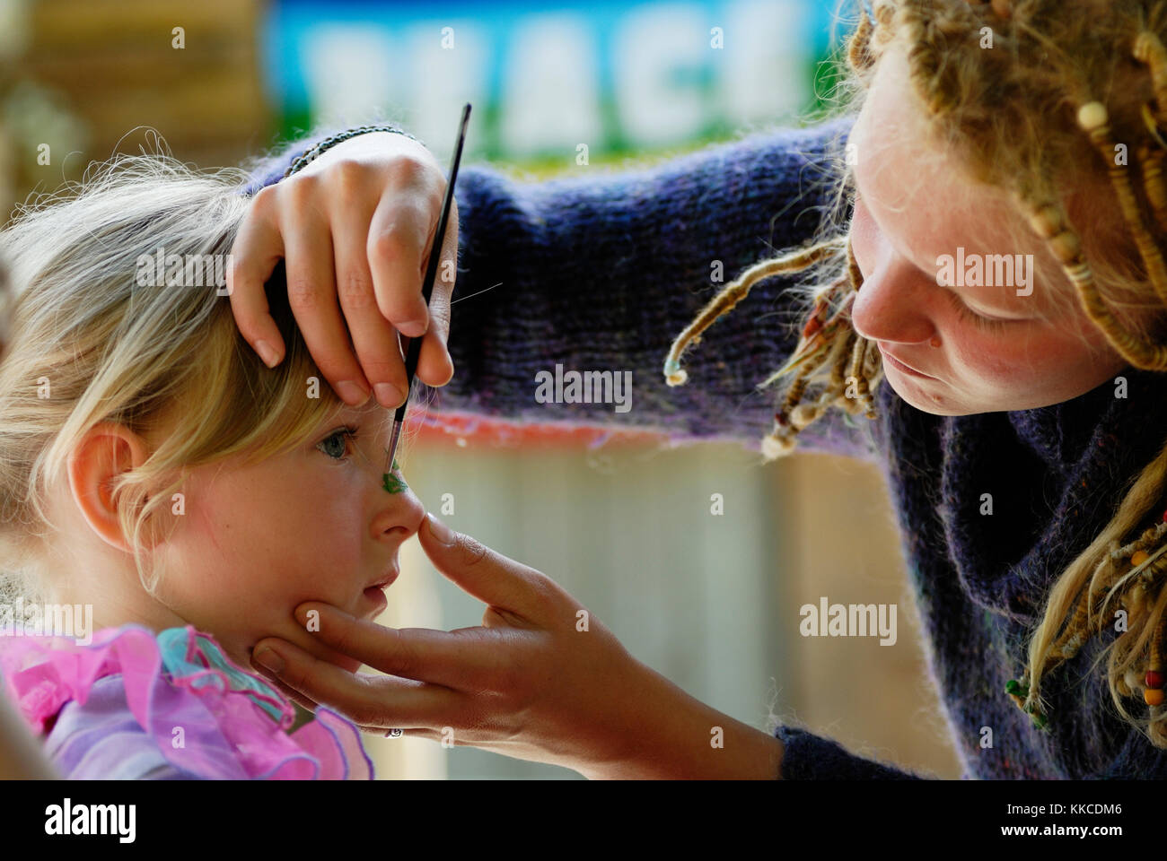 Young woman painting the face of a girl child,with Peace flag in background, Wales,UK. Stock Photo