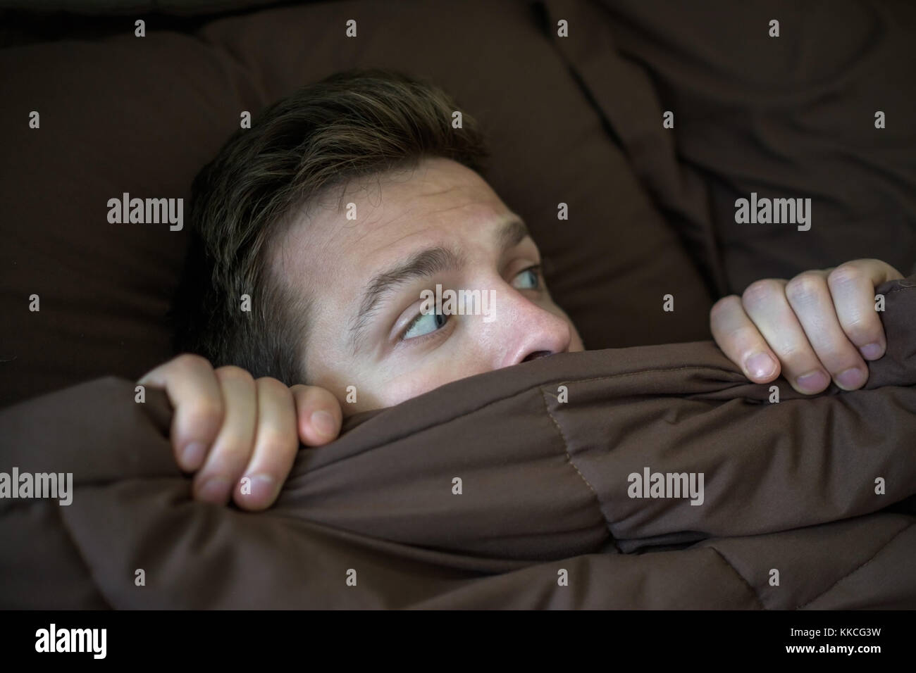 Caucasian young man hiding in bed under the blanket at home. Stock Photo