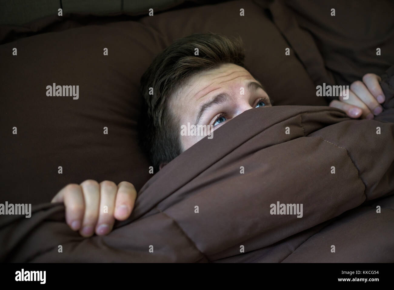 Caucasian young man hiding in bed under the blanket at home. Stock Photo