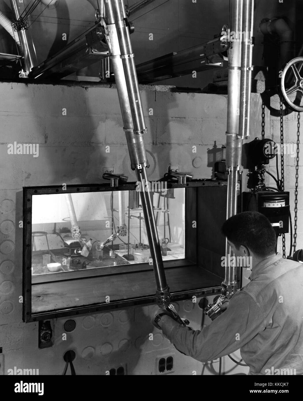 In the Physics of Solids Building at Oak Ridge National Laboratory, a step in preparation of a solid sample of extremely radioactive material for analysis is concluded as the scientist, separated from his work by concrete barrier and liquid-filled porthole, uses manipulators, or 'mechanical hands, ' to wash his equipment. Courtesy Department of Energy. 1952. Stock Photo