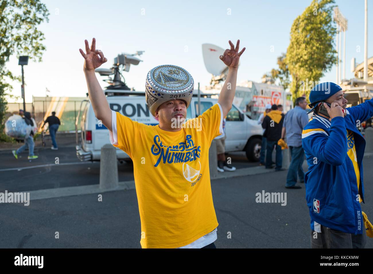 Following Game 2 of the National Basketball Association (NBA) Finals between the Golden State Warriors and the Cleveland Cavaliers, a fan of the Warriors wears a customized hat made to resemble a championship ring and celebrates his team's victory while making 'okay' signs with his hands, Oakland, California, June 5, 2016. Stock Photo