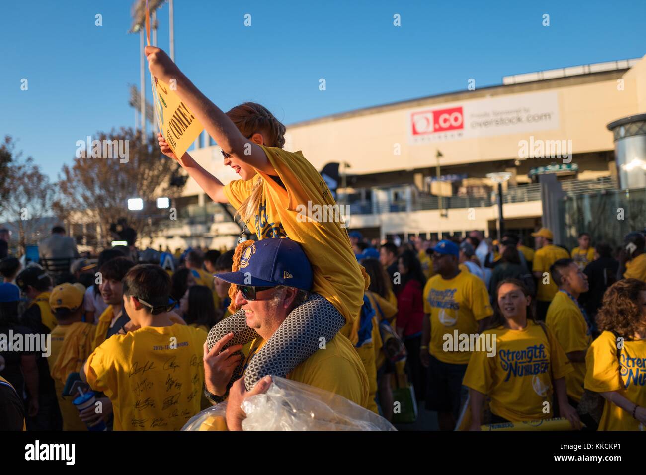 Following Game 2 of the National Basketball Association (NBA) Finals between the Golden State Warriors and the Cleveland Cavaliers, a young fan of the Warriors sits on her father's shoulders and holds a sign, Oakland, California, June 5, 2016. Stock Photo