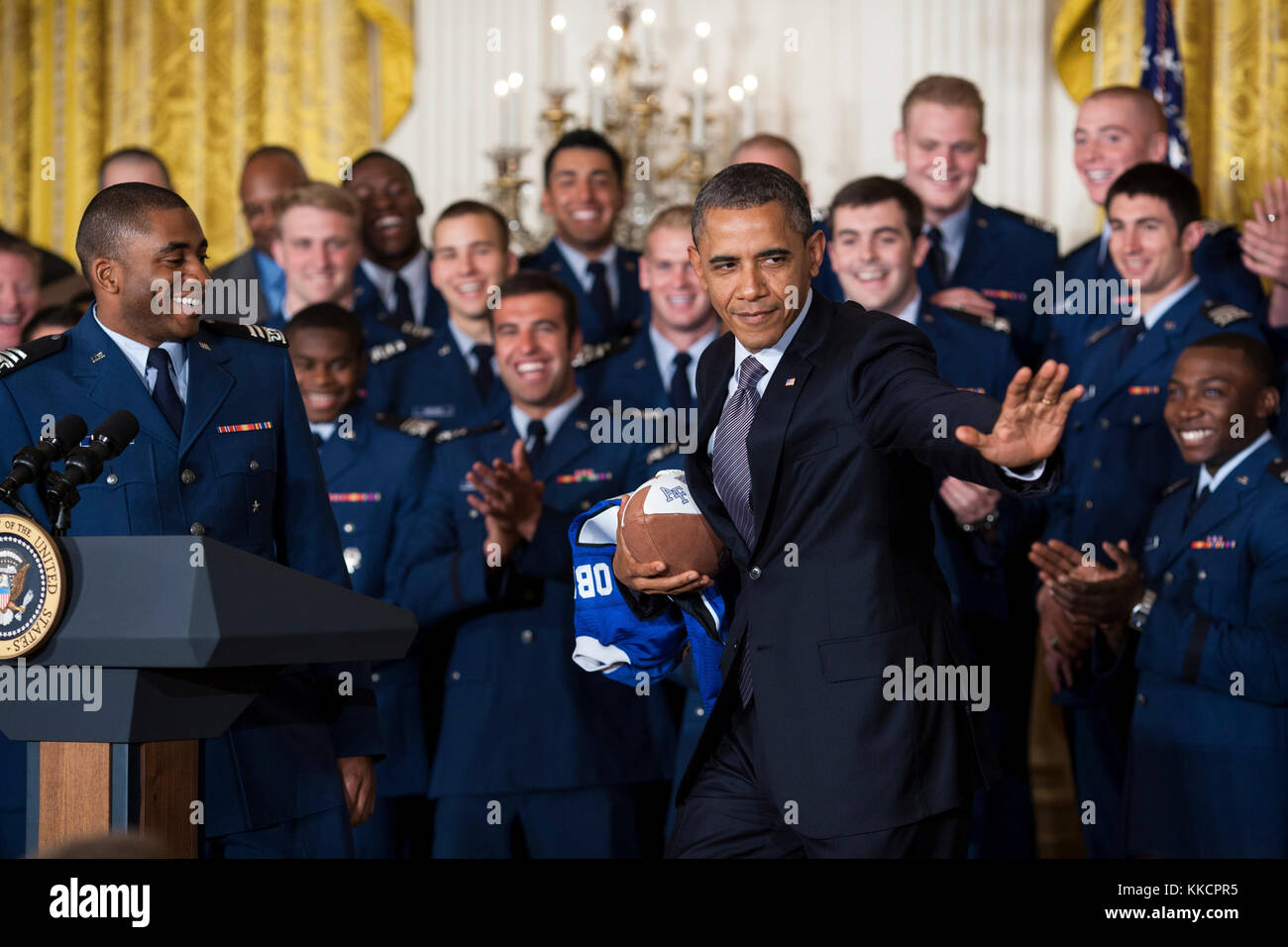 President Barack Obama strikes the Heisman pose after accepting a football from quarterback Tim Jefferson, left, during the Commander-in-Chief Trophy presentation to the United States Air Force Academy football team in the East Room of the White House, April 23, 2012. The Air Force beat Army and Navy in 2011 to claim the trophy for the 18th time. (Official White House Photo by Pete Souza)  This official White House photograph is being made available only for publication by news organizations and/or for personal use printing by the subject(s) of the photograph. The photograph may not be manipul Stock Photo