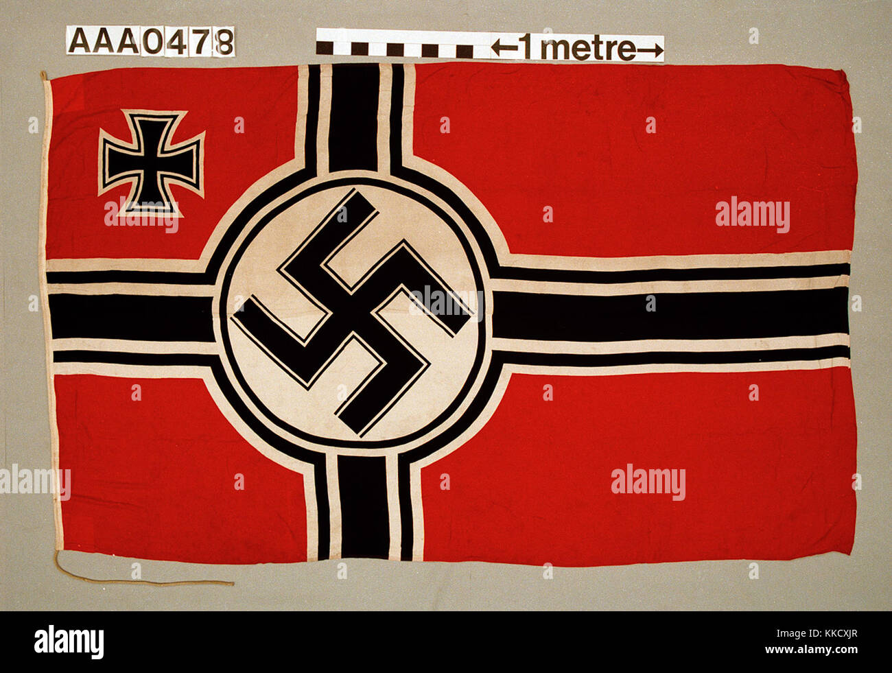 Nazi German naval ensign, 1935-45 pattern. Stencilled on the hoist is: 'REICHSKRIEGSFLG 300 X 500 PLÜSCHWEBER GREFRATH'. The flag is made of machine sewn cotton with the design printed onto the fabric. A rope is attached to hoist the flag. Design:  Red field with off centre black cross, edged white/black/white. It has a white disc in the centre with a black swastika. In the canton an iron cross, edged white/black/white.  AAA0478 Nazi German naval ensign (1935-1945) RMG RP-33-4-5 Stock Photo
