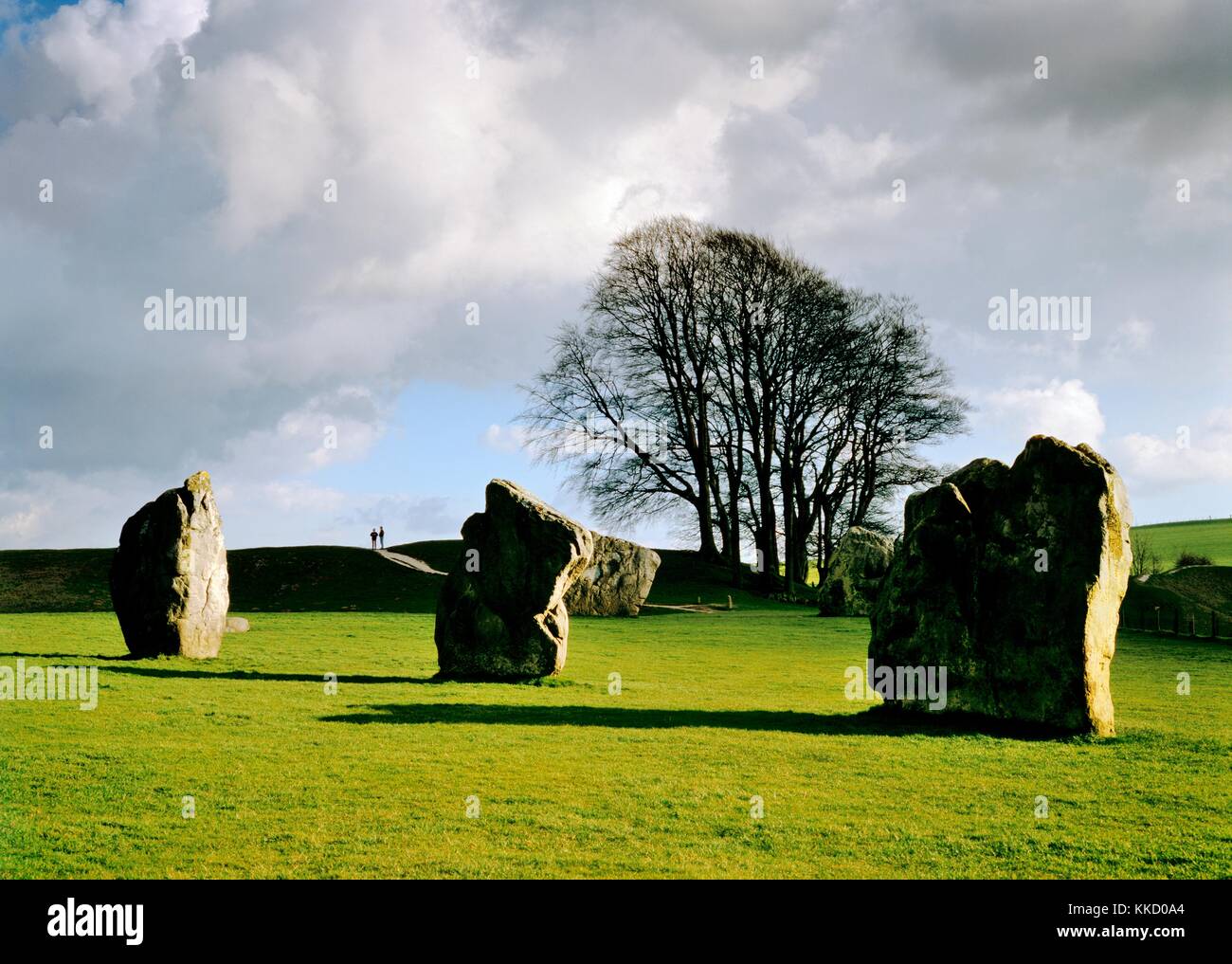 People on encircling earthwork beyond 3 of the standing stones of huge prehistoric stone circle of Avebury, Wiltshire, England. Stock Photo