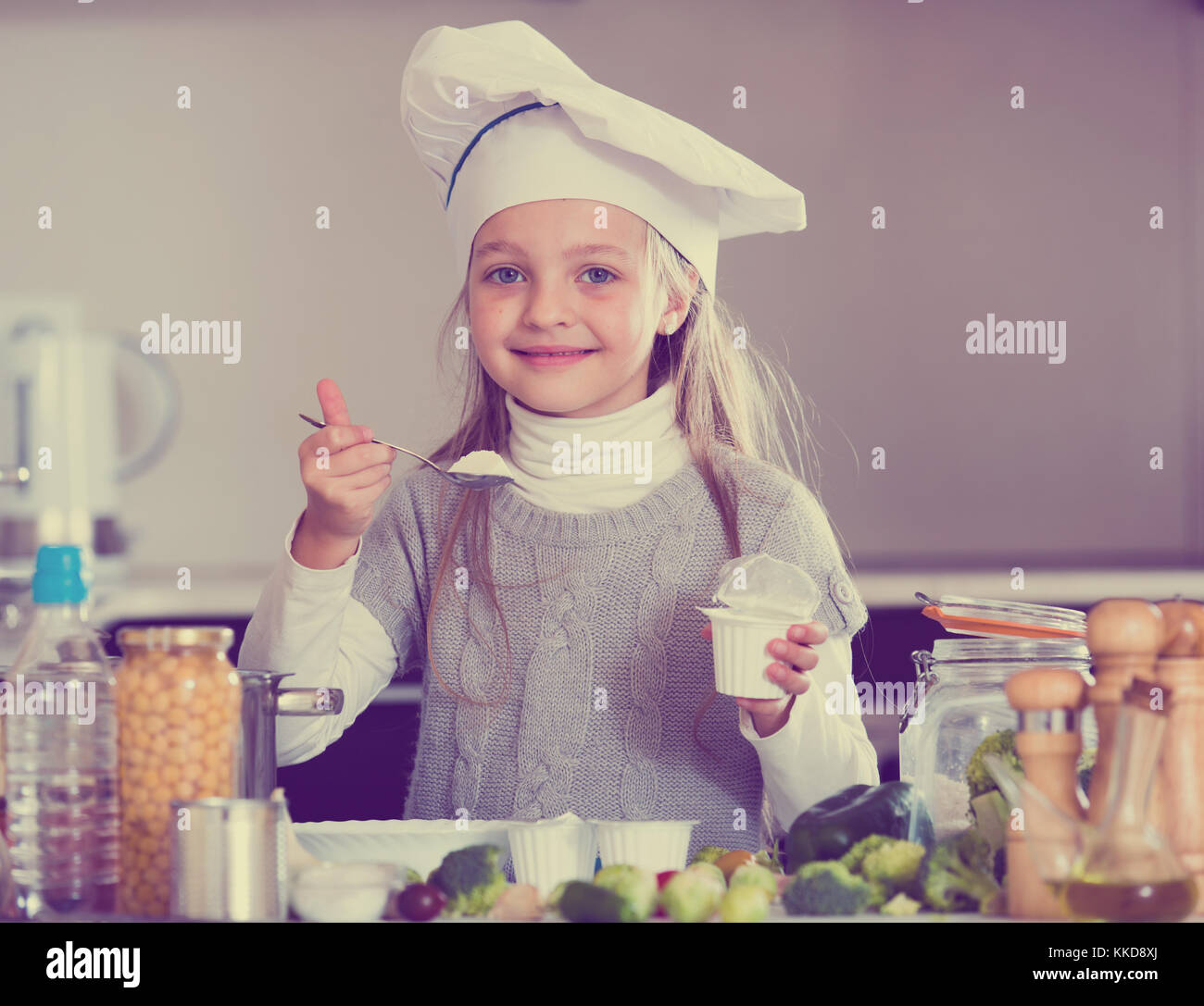 Little girl eating healthy yoghurt in kitchen and smiling Stock Photo