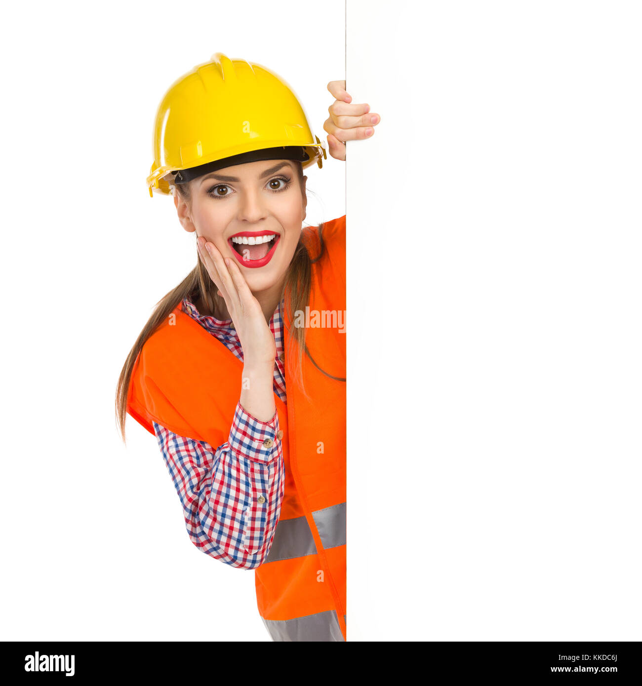 Excited young woman in yellow hardhat, orange reflective vest and lumberjack shirt posing with big banner with mouth open and hand on chin. Waist up s Stock Photo
